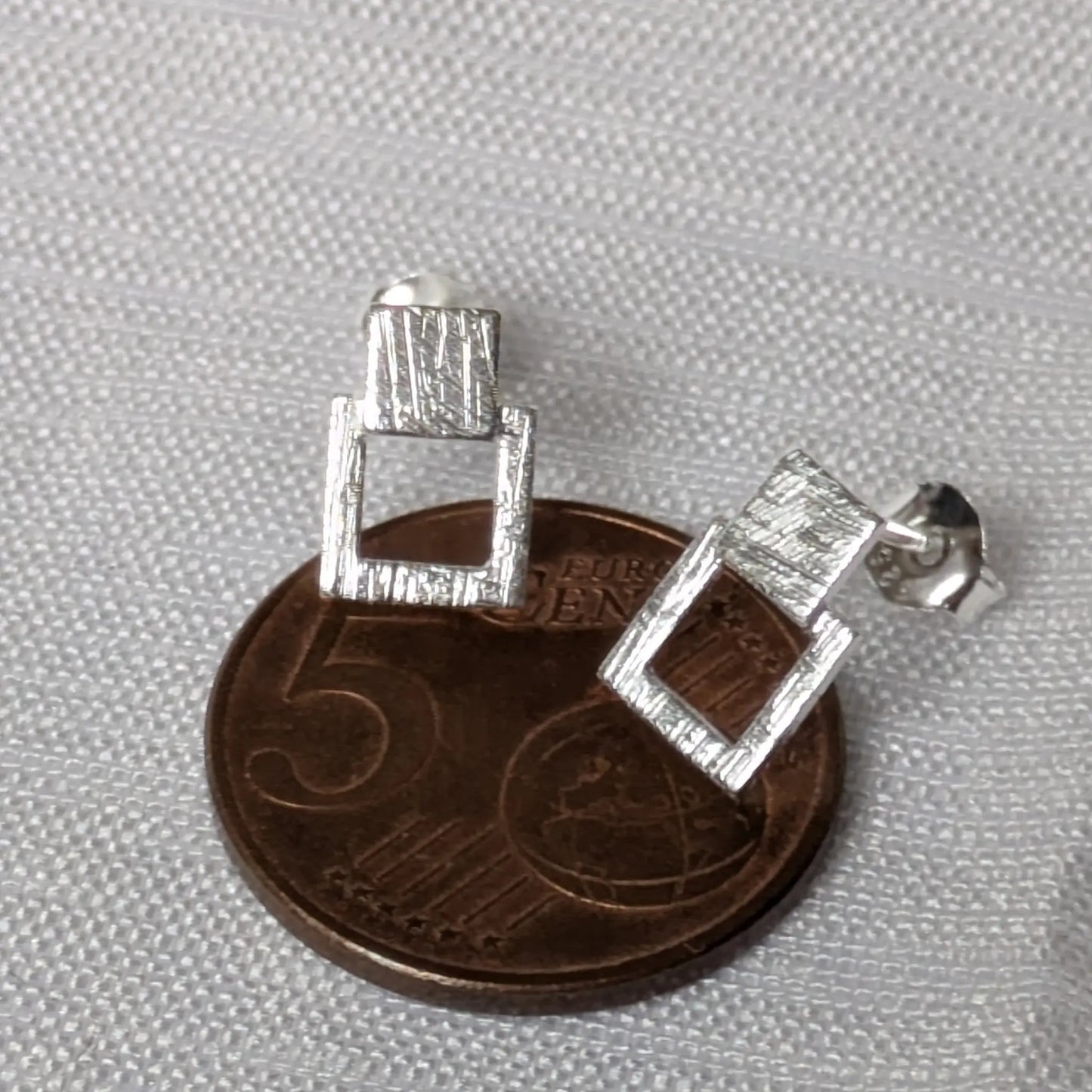 Größenvergleich der geometrischen Silber-Ohrstecker auf einer Münze.