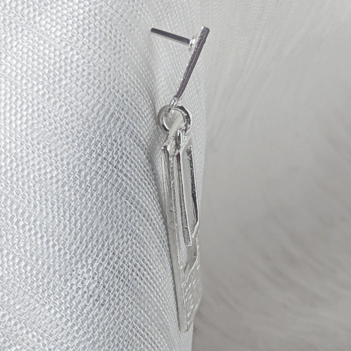 Seitenansicht der hängenden Silber Ohrstecker, die den geraden Befestigungsstift und die flache Form der Rechtecke illustriert.

