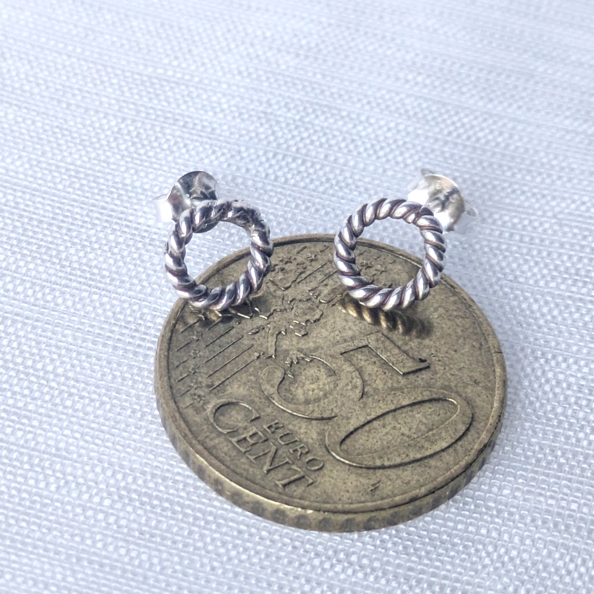 Detailaufnahme silberne Ohrsteckers mit strukturierter Oberfläche auf 50-Cent Münze