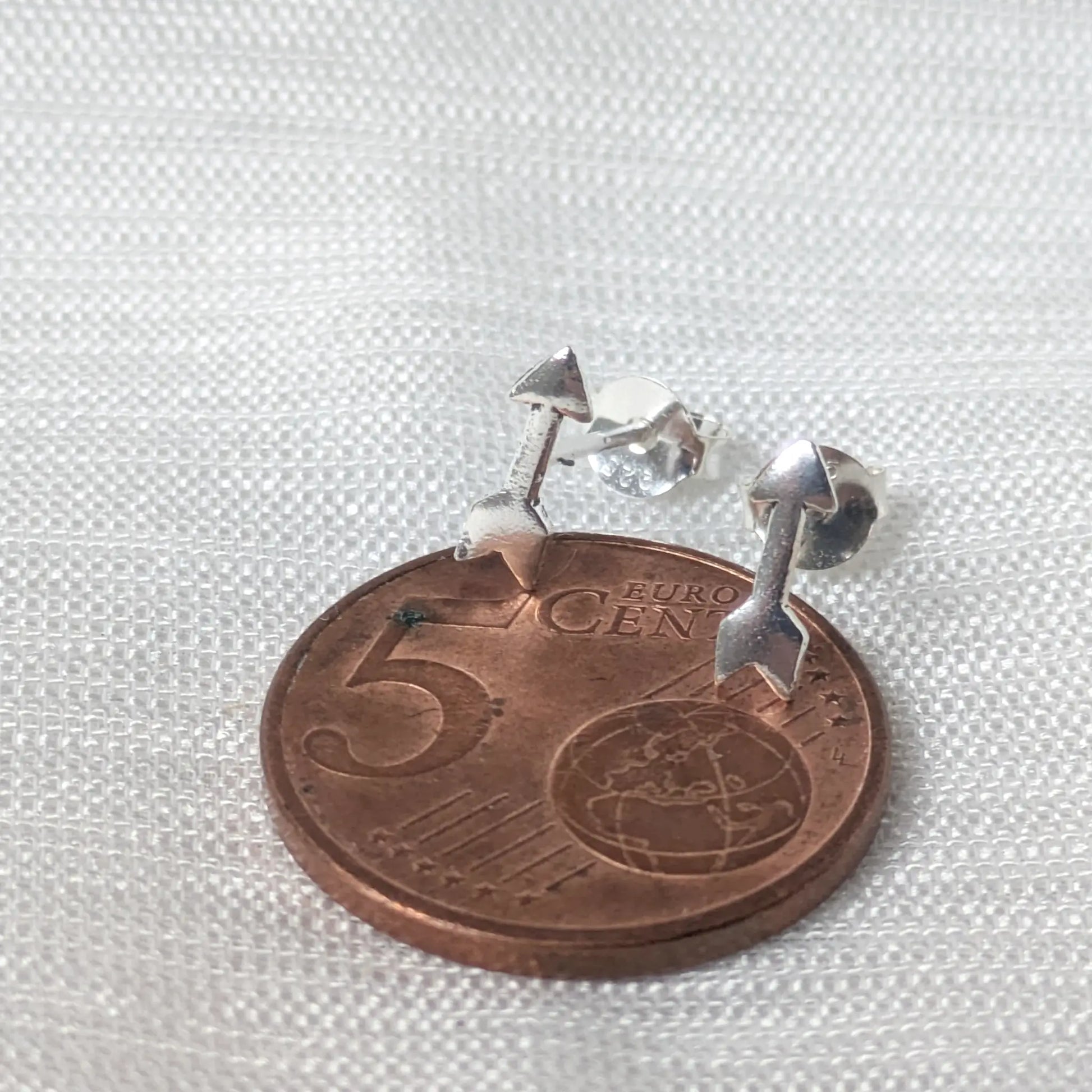 Größenvergleich: Filigrane Pfeil-Ohrringe aus Silber platziert auf einer 5-Cent-Münze zur Verdeutlichung der zierlichen Maße.