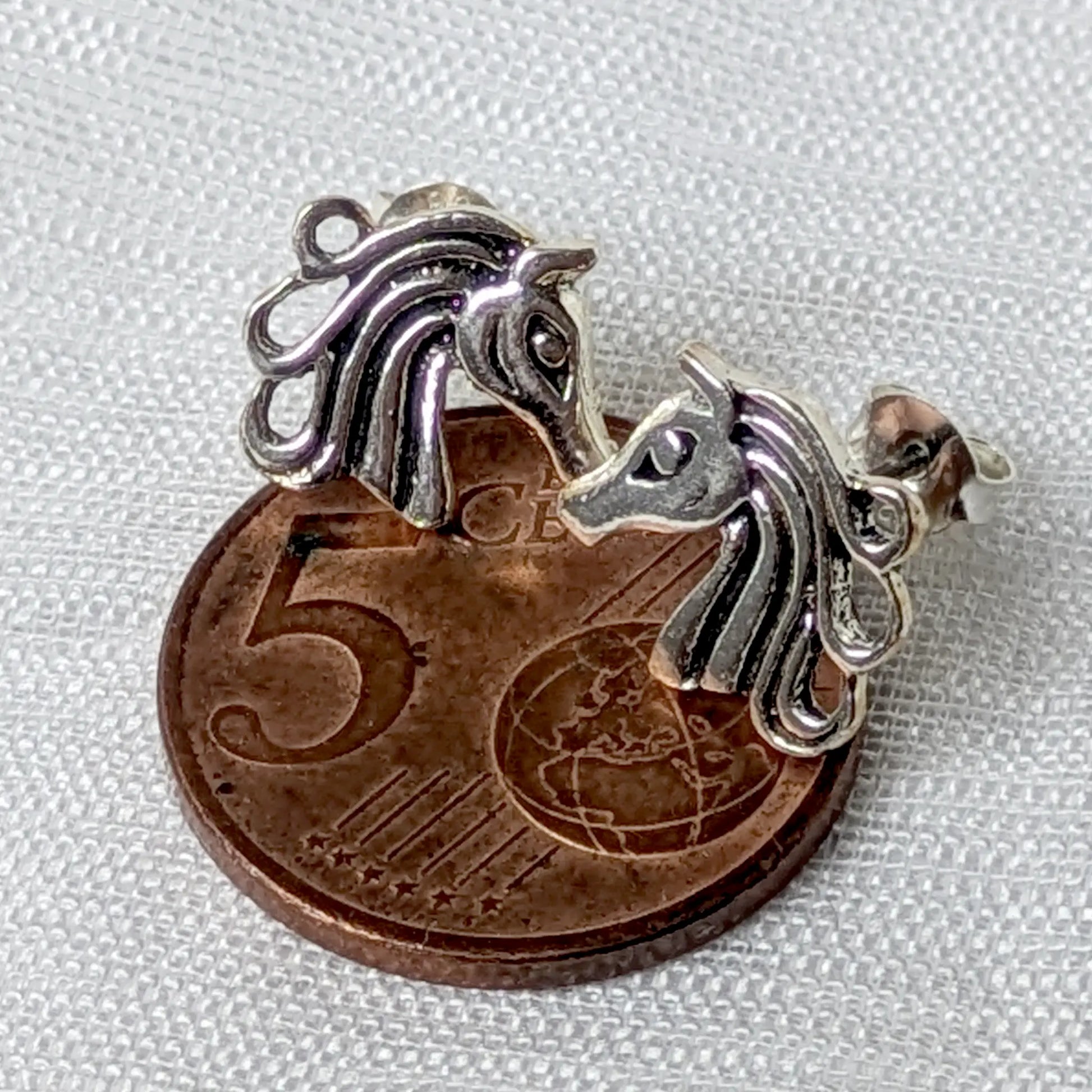 Größenvergleich der zierlichen Pferdekopf-Ohrstecker aus Silber auf einer 5-Cent-Münze.