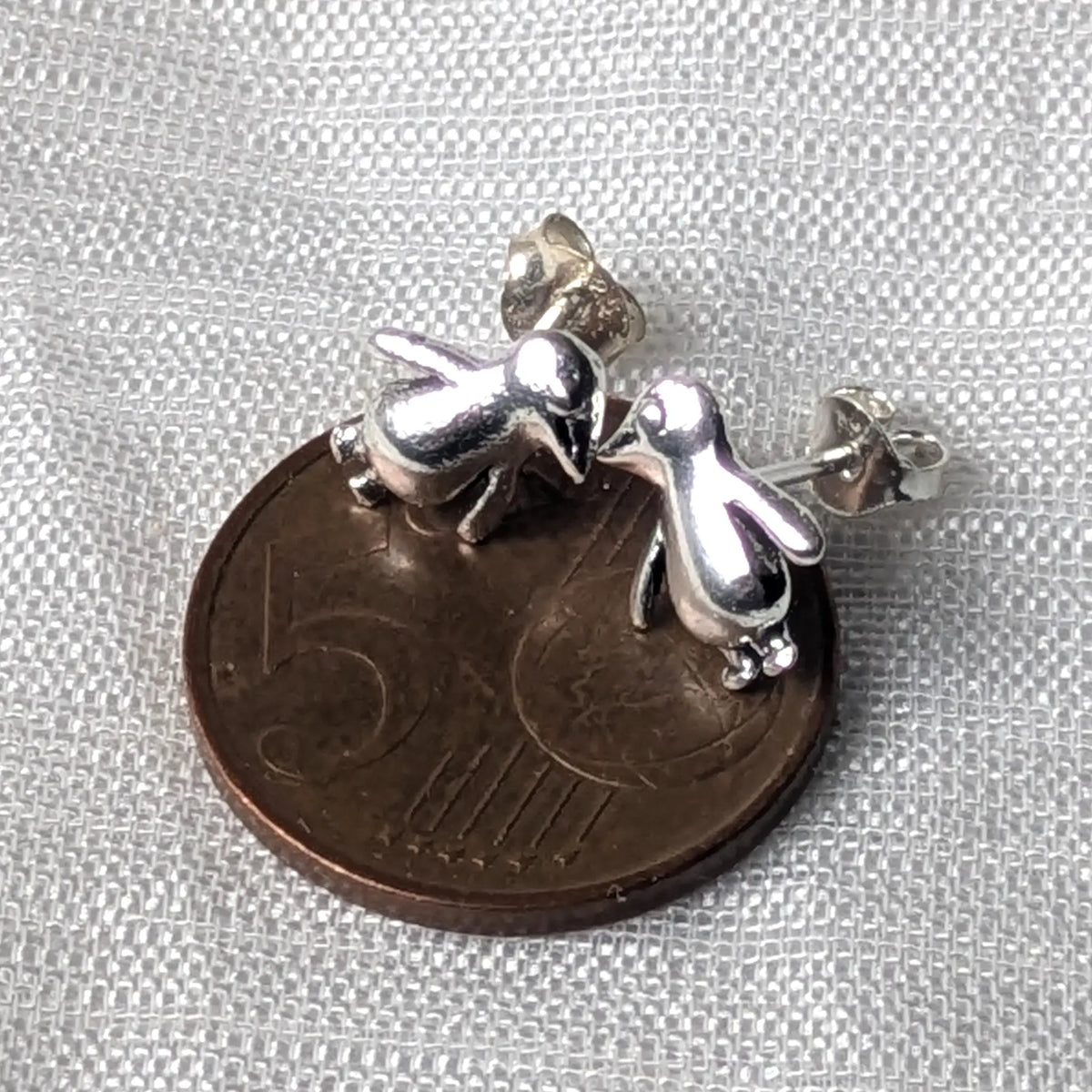 Größenvergleich der filigranen Pinguin-Silberohrstecker, die zur Demonstration ihrer zierlichen Maße flach auf einer 5-Cent-Münze liegen.
