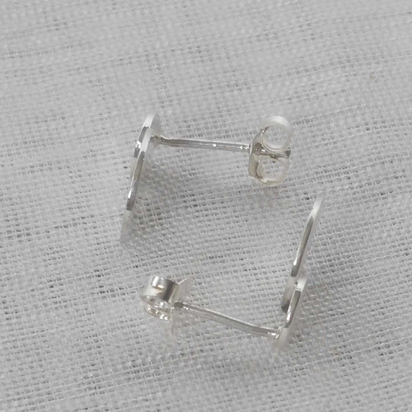Seitenansicht der flachen Silber-Ohrstecker zur Veranschaulichung der Stecker-Stifte und der glatten, polierten Oberfläche.