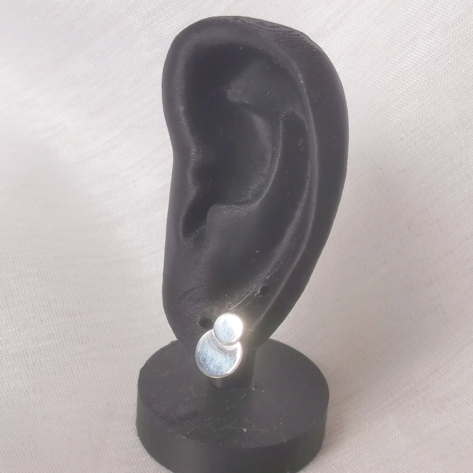 Größenbeispiel: Ein glänzender Doppel-Plättchen Ohrstecker aus 925 Silber getragen an einem schwarzen Ohr-Display zur Veranschaulichung der Passform.