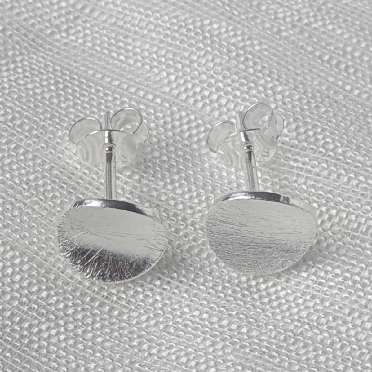 Frontalansicht der kreisförmigen Silberohrstecker, die die markante, kratzmatte Textur der runden Scheibe zeigt.
