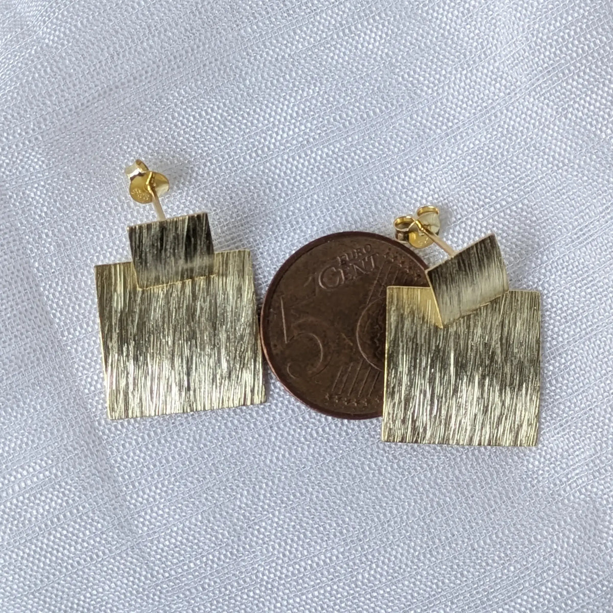 Größenvergleich der vergoldeten eckigen Statement-Ohrringe, liegend auf einer 5-Cent-Münze zur Veranschaulichung der Dimensionen.
