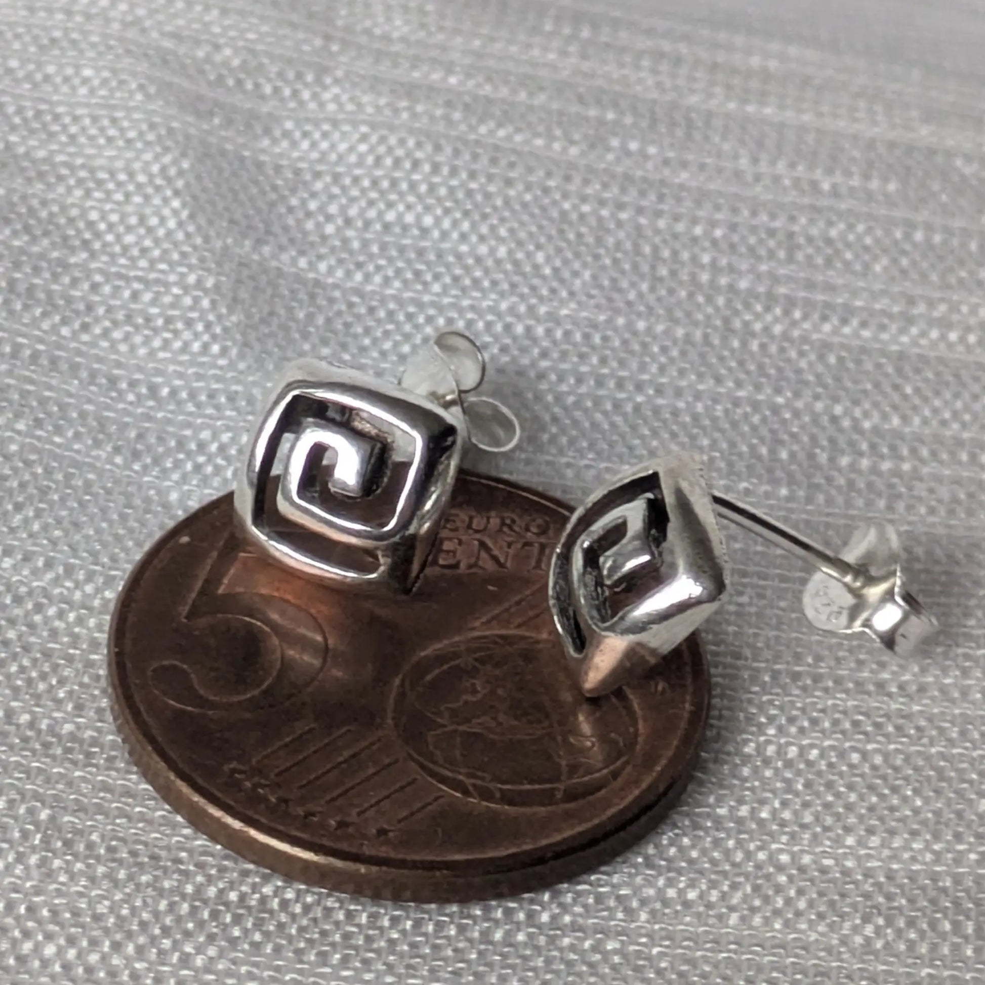 Größenvergleich der quadratischen Mäander-Ohrstecker auf einer 5-Cent-Münze.