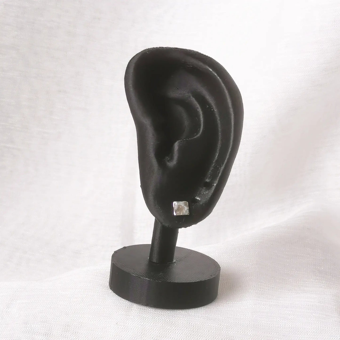 Die quadratischen Silber-Ohrstecker präsentiert an einem matten, schwarzen Ohr-Display zur Veranschaulichung der Proportionen
