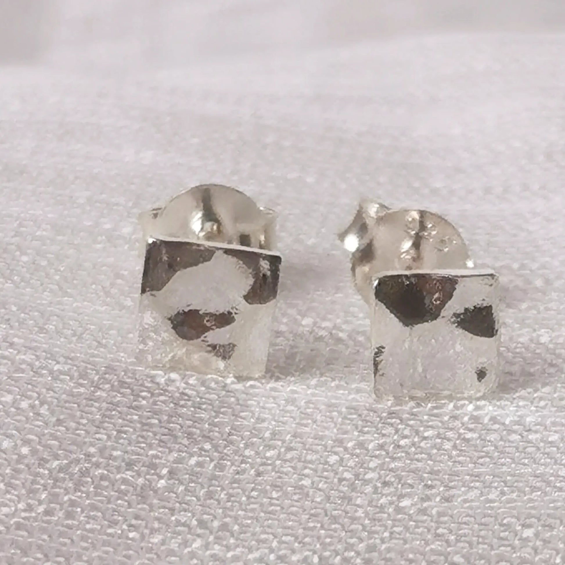 Frontale Ansicht der eckigen Sterling Silber Ohrringe in Hammerschlag-Optik auf einer strukturierten, hellen Unterlage.