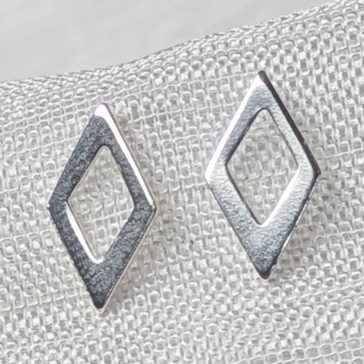 Nahaufnahme von geometrischen 925 Silber Ohrsteckern in offener Rautenform mit strukturierter Oberfläche und glänzend polierten Kanten.
