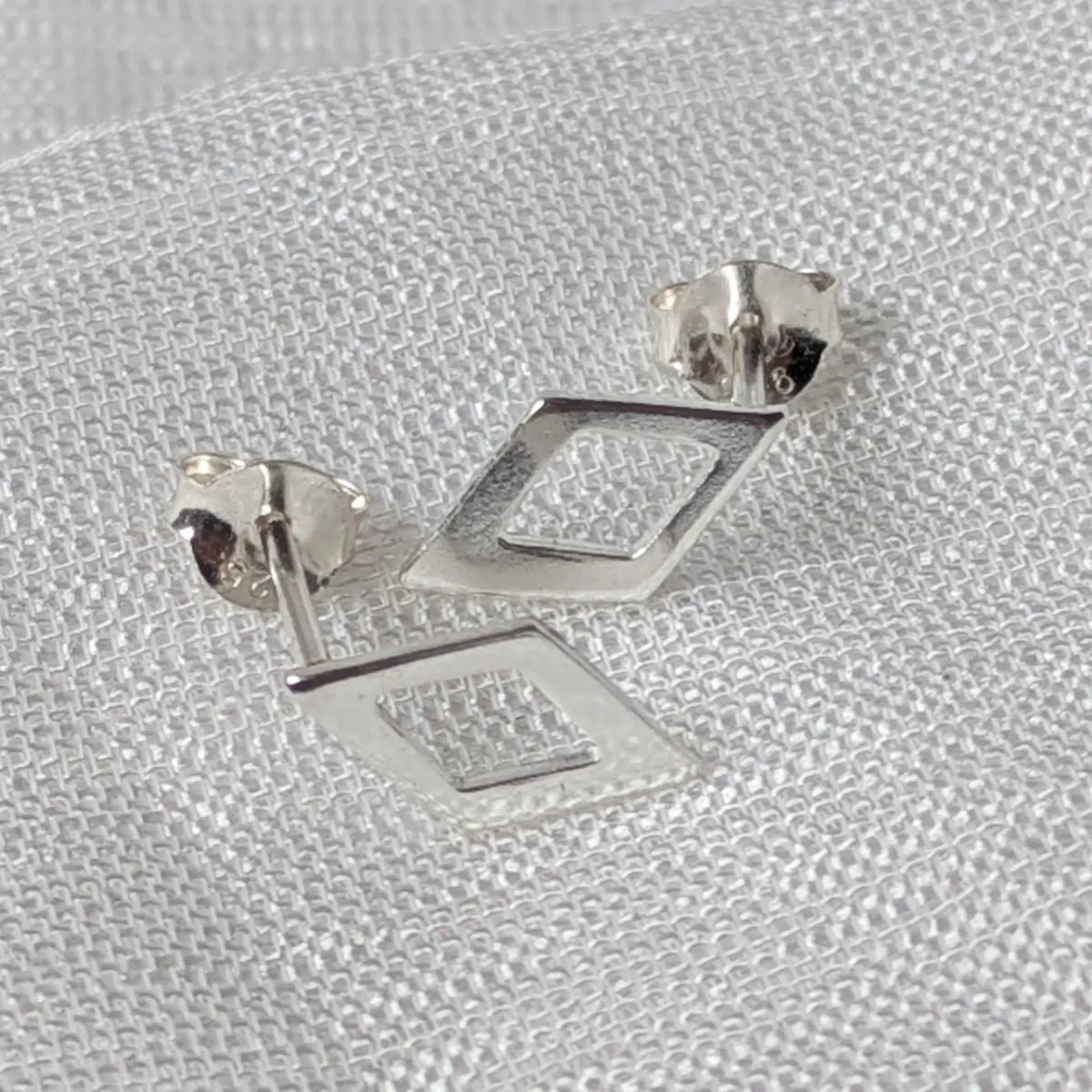 Frontalansicht der Rauten-Silberohrstecker, die das durchbrochene, eckige Design und die Materialtextur deutlich zeigt.
