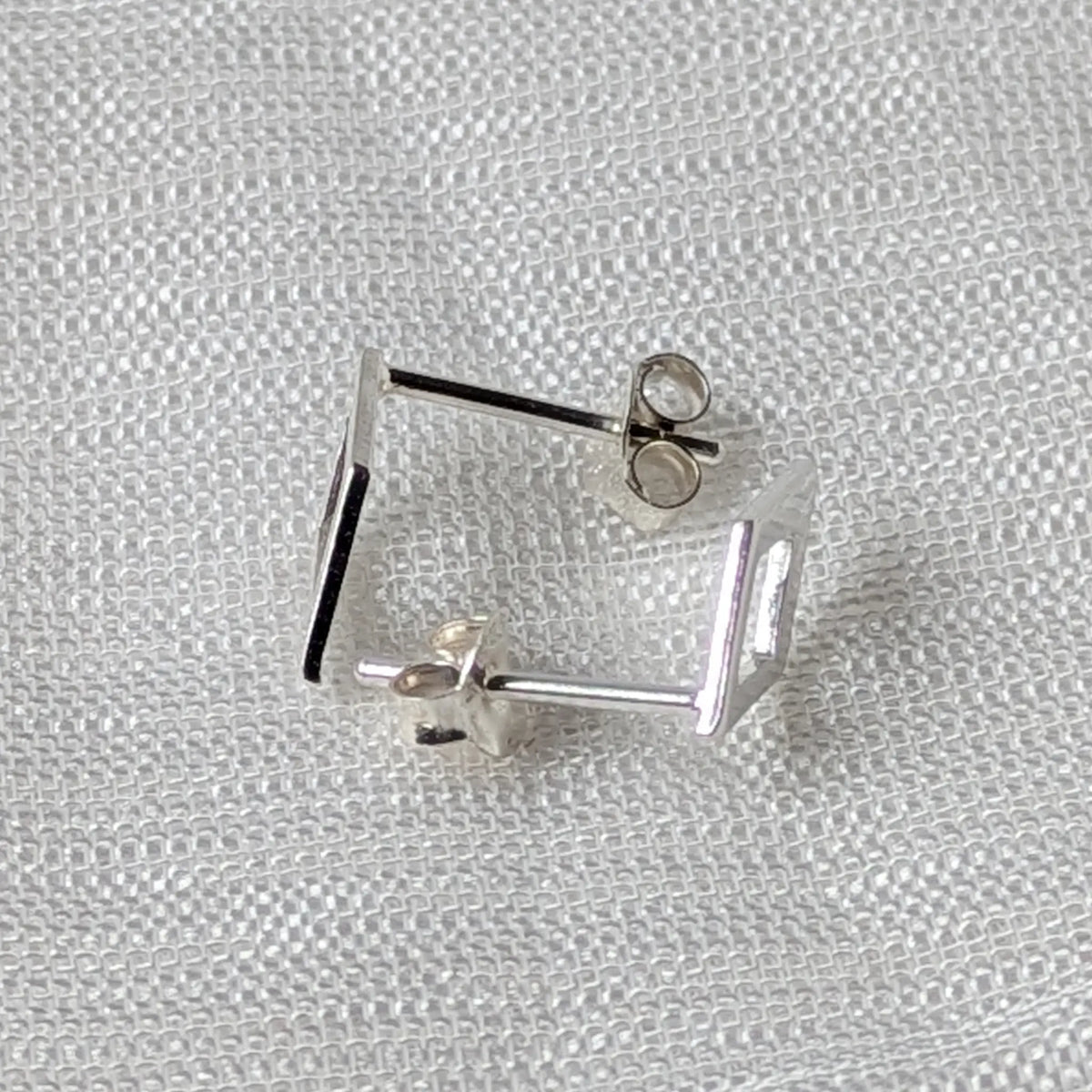 Seitenansicht der flachen Rauten-Ohrstecker aus Silber, die das minimalistische, eng anliegende Profil verdeutlicht.