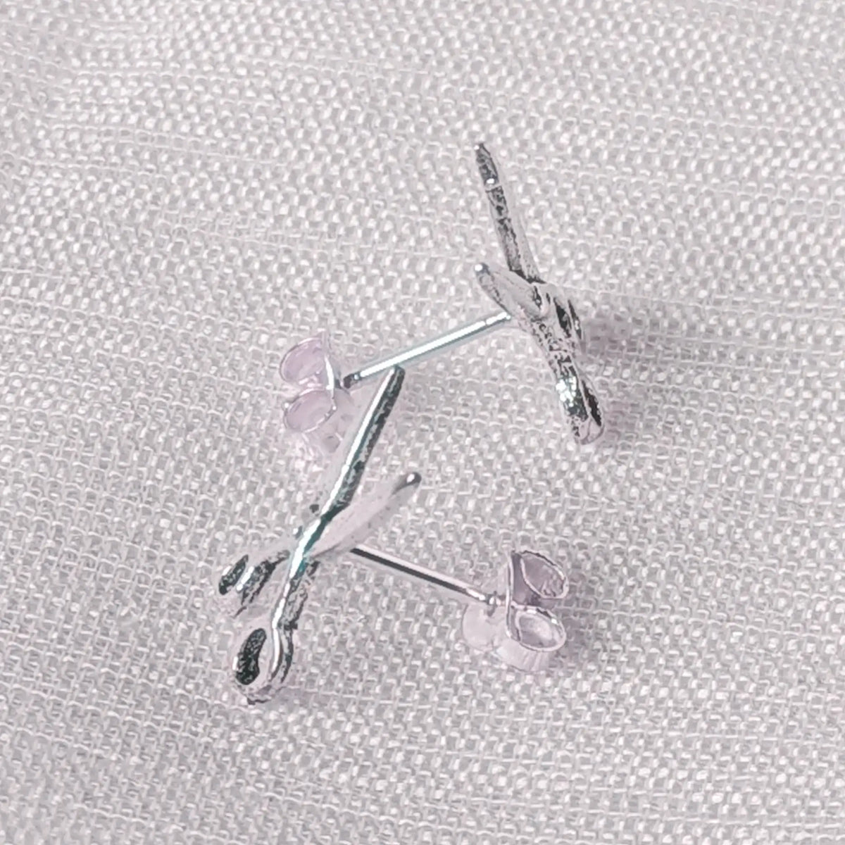 Seitliche Perspektive der flachen Silberohrstecker mit detailliertem Scheren-Motiv.