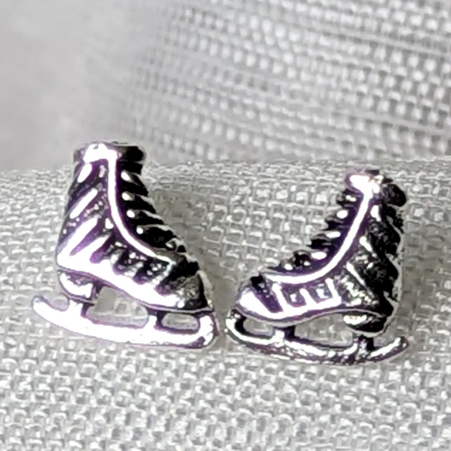 Detailreiche Nahaufnahme von zwei Schlittschuh Ohrsteckern aus 925 Sterling Silber mit geschwärzten Details an Schnürung und Kufen.
