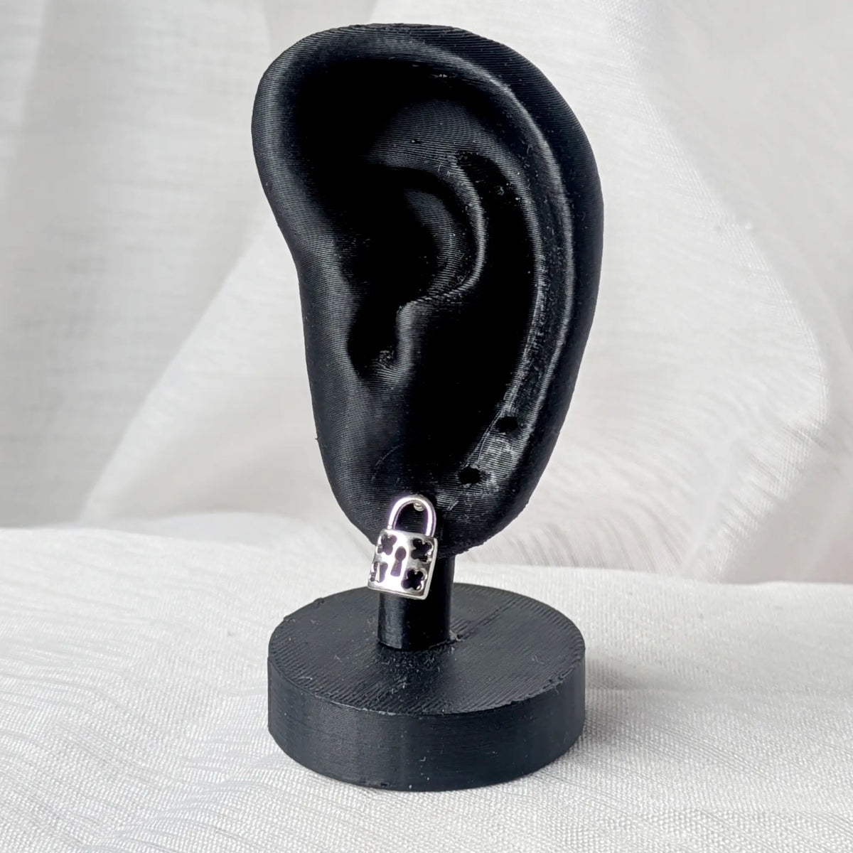 Der silberne Vorhängeschloss-Ohrstecker, dezent getragen am Ohrläppchen eines schwarzen 3D-Modell-Ohrs zur Größenveranschaulichung