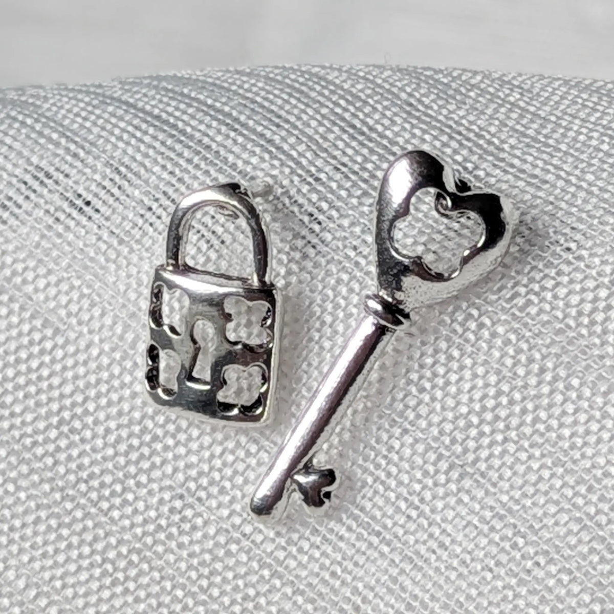 Nahaufnahme von asymmetrischen 925 Silber Ohrsteckern, die ein Vorhängeschloss und einen Schlüssel mit feinen Ausstanzungen zeigen.