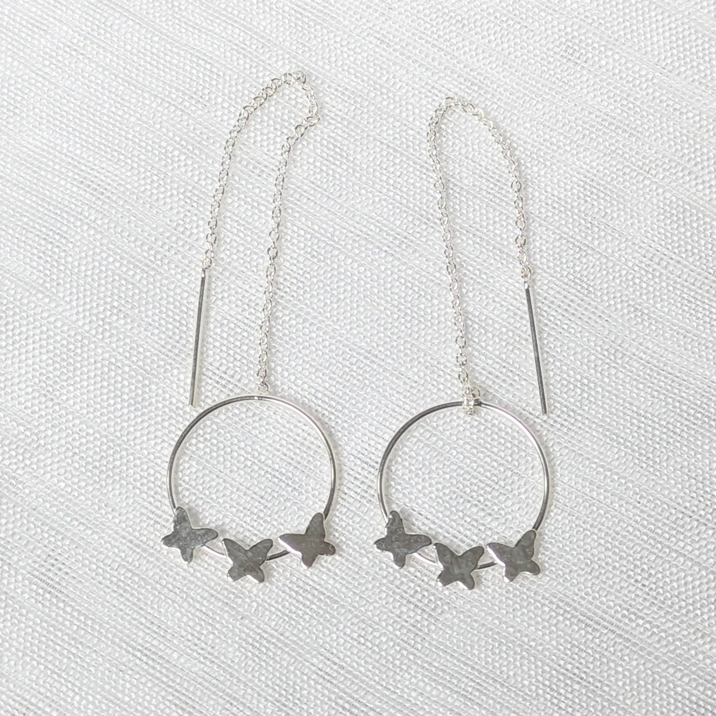 Nahaufnahme von filigranen 925 Silber-Durchziehohrringen mit drei kleinen Schmetterlingen auf einem runden Element.