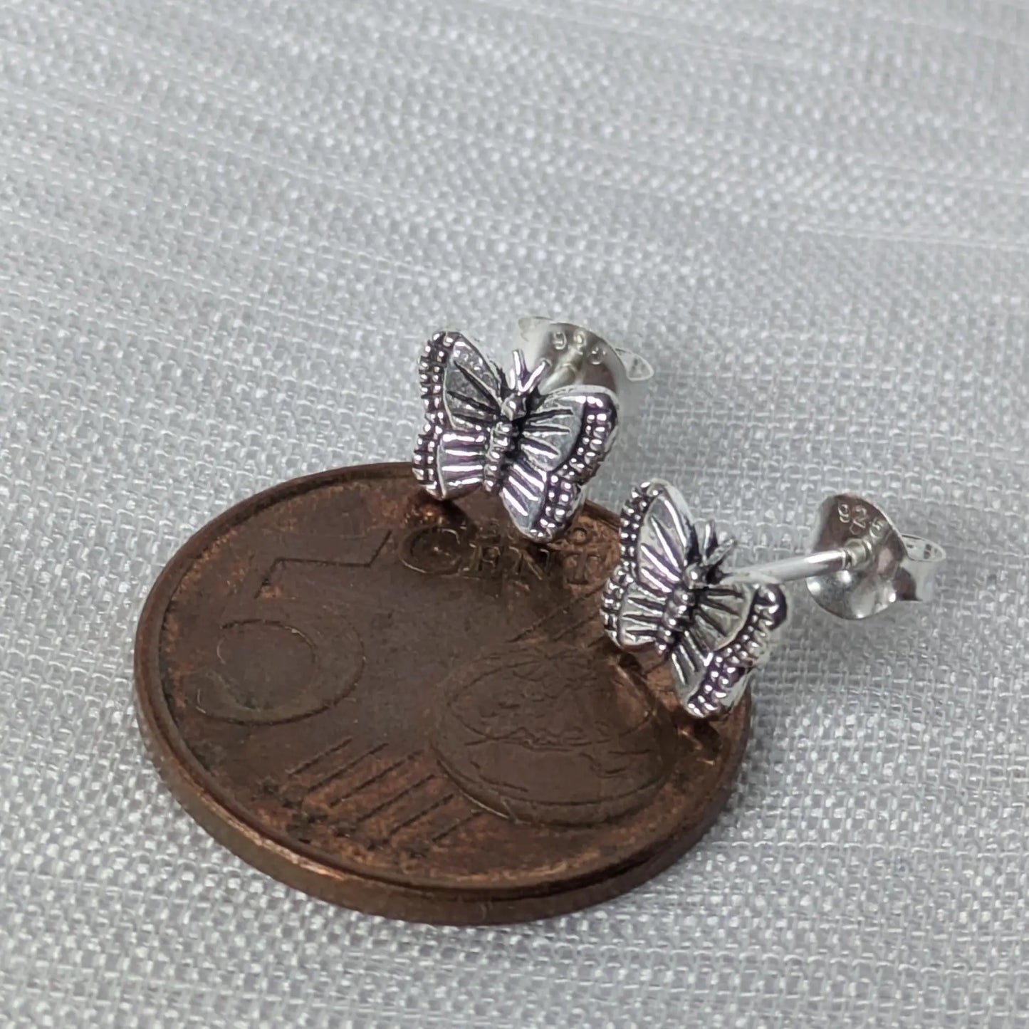 Größenvergleich der Schmetterling Ohrstecker aus Silber neben einer 5-Cent-Münze.