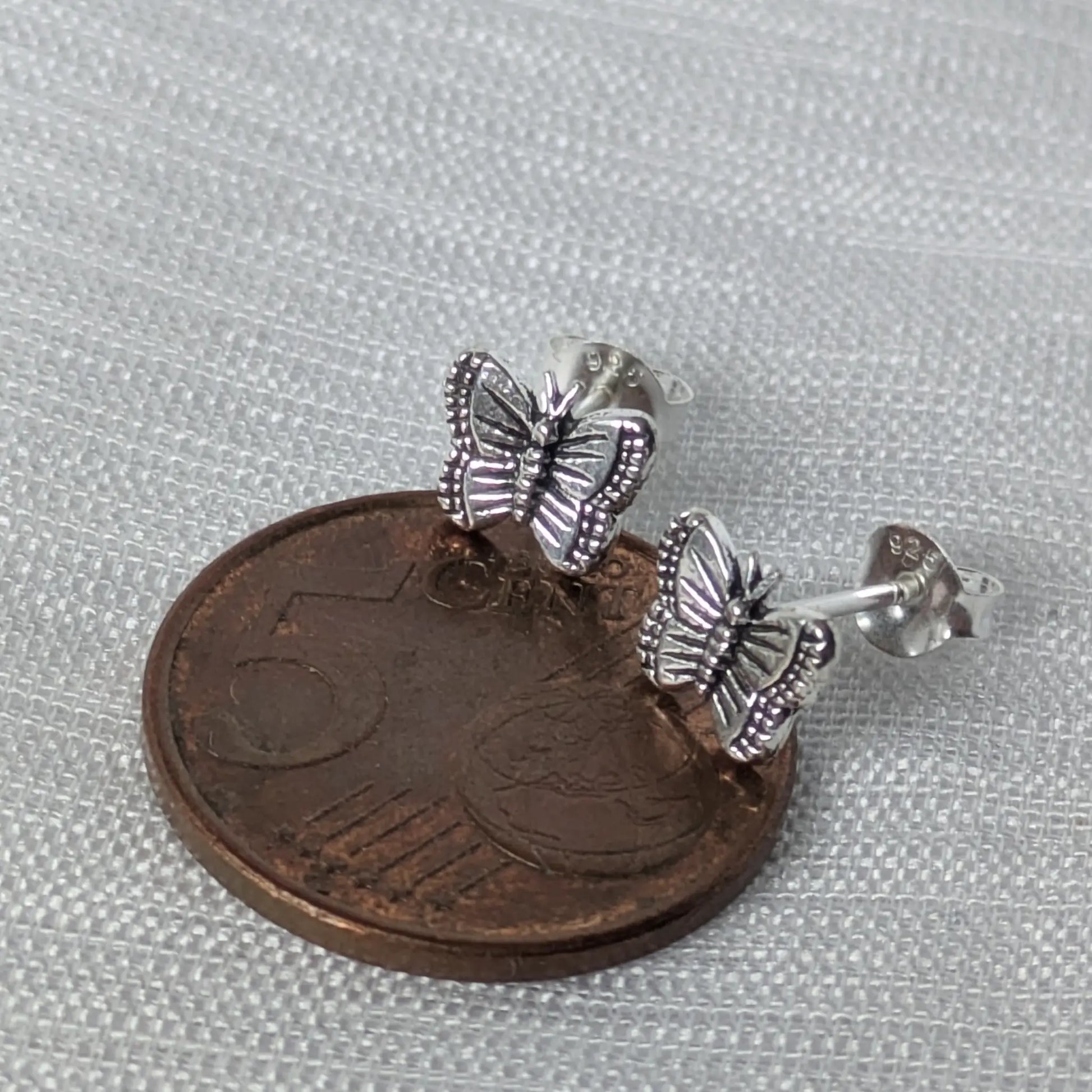 Größenvergleich der Schmetterling Ohrstecker aus Silber neben einer 5-Cent-Münze.