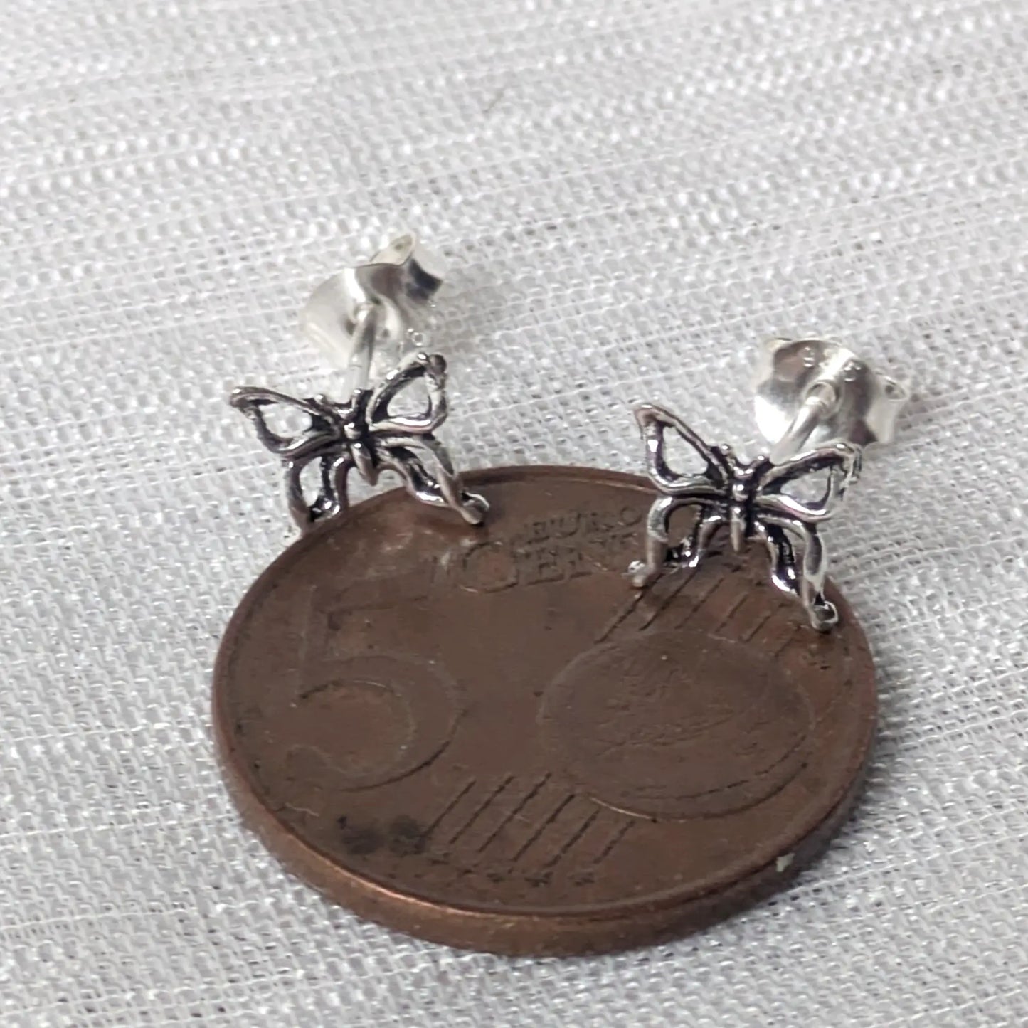 Größenvergleich von silbernen Schmetterlings-Ohrsteckern auf einer 5-Cent-Münze
