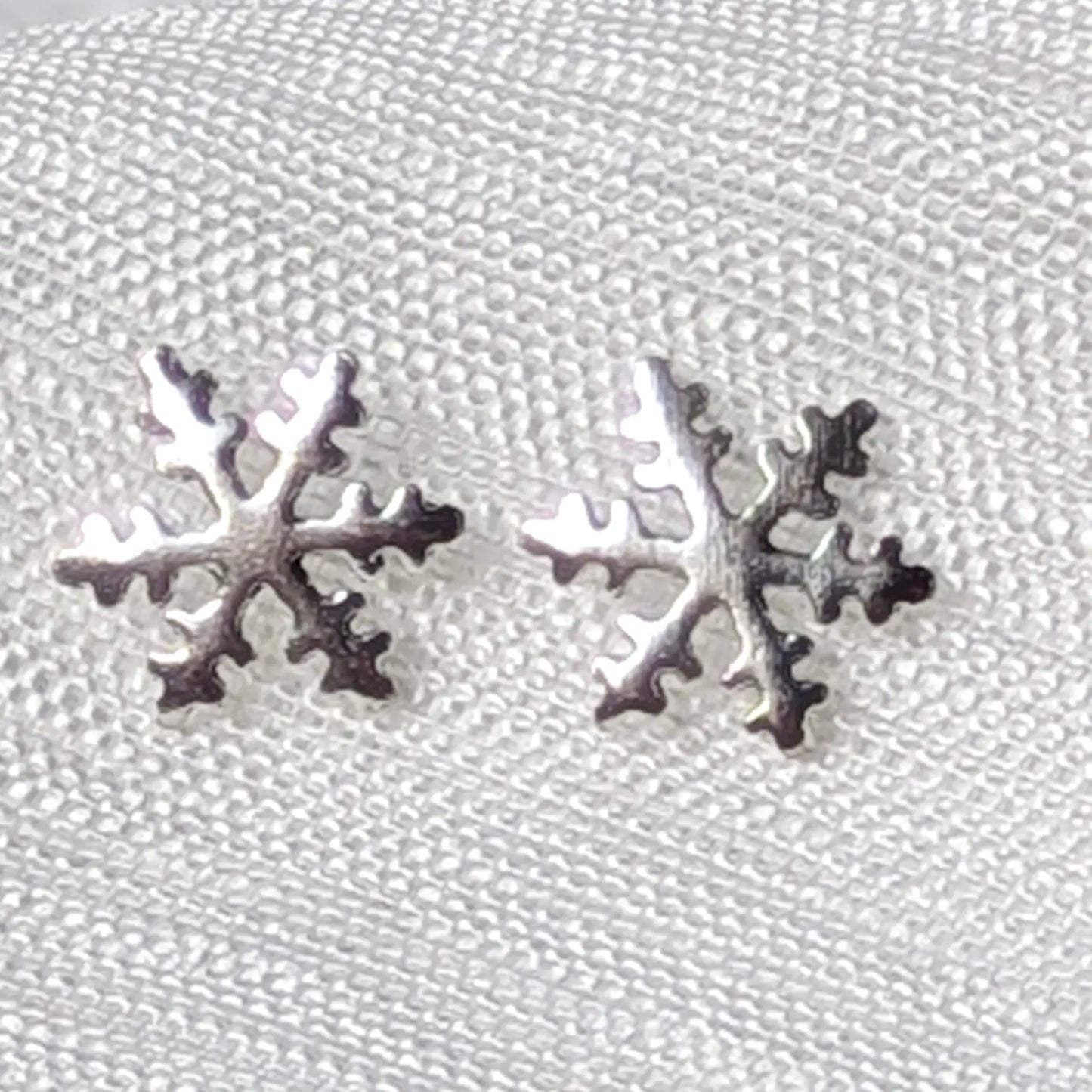 Detailreiche Nahaufnahme von zwei hochglanzpolierten Schneeflocken Ohrsteckern aus echtem 925 Sterling Silber.