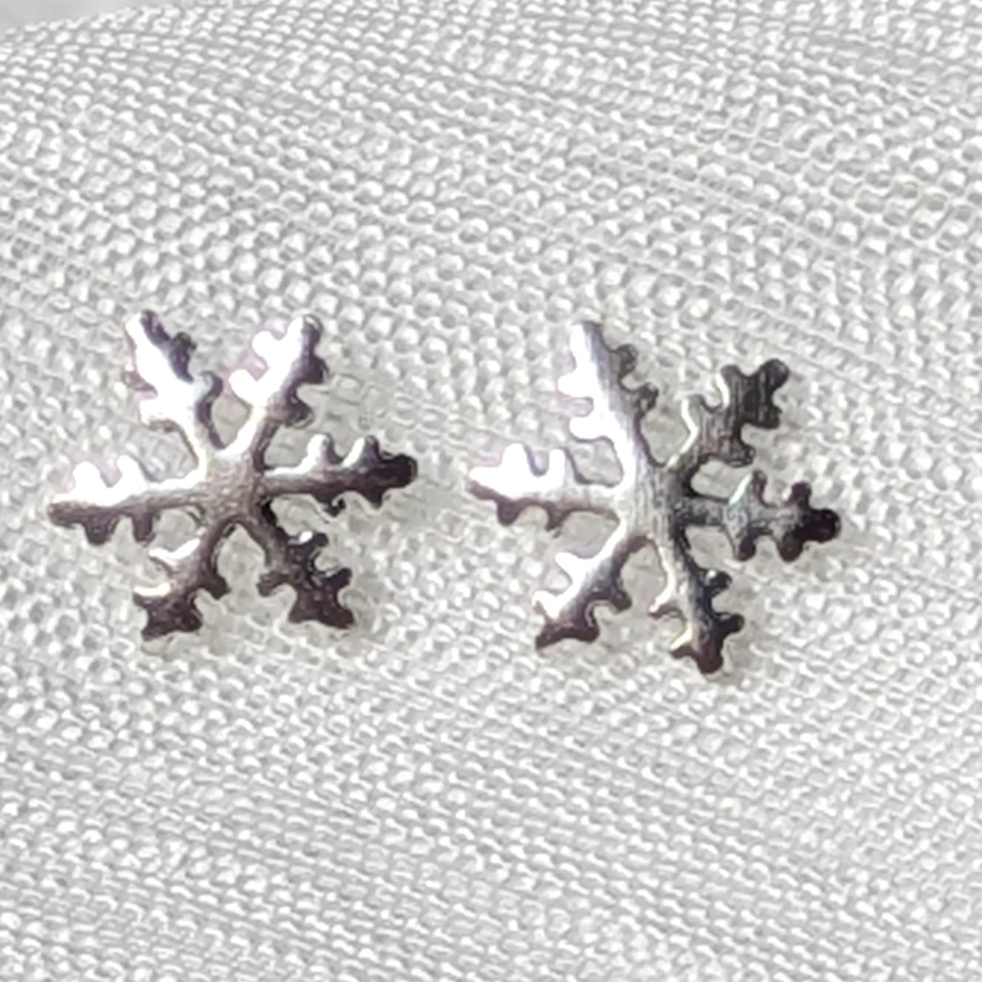 Detailreiche Nahaufnahme von zwei hochglanzpolierten Schneeflocken Ohrsteckern aus echtem 925 Sterling Silber.