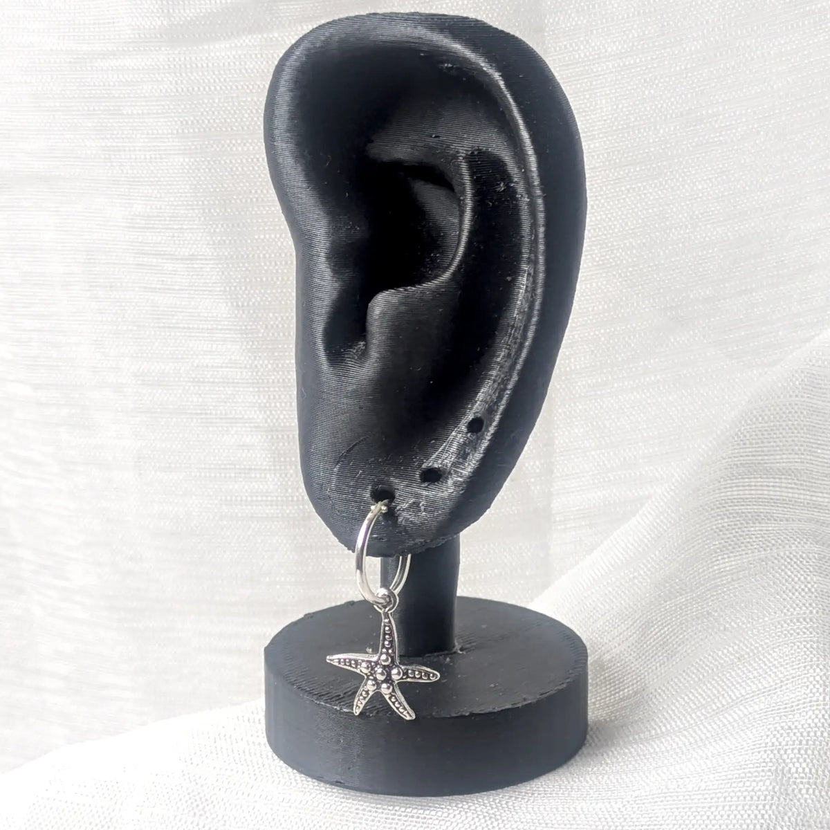Eine Silber-Creole mit Seestern-Anhänger präsentiert an einem schwarzen 3D-Ohr-Display zur Veranschaulichung der Tragelänge.