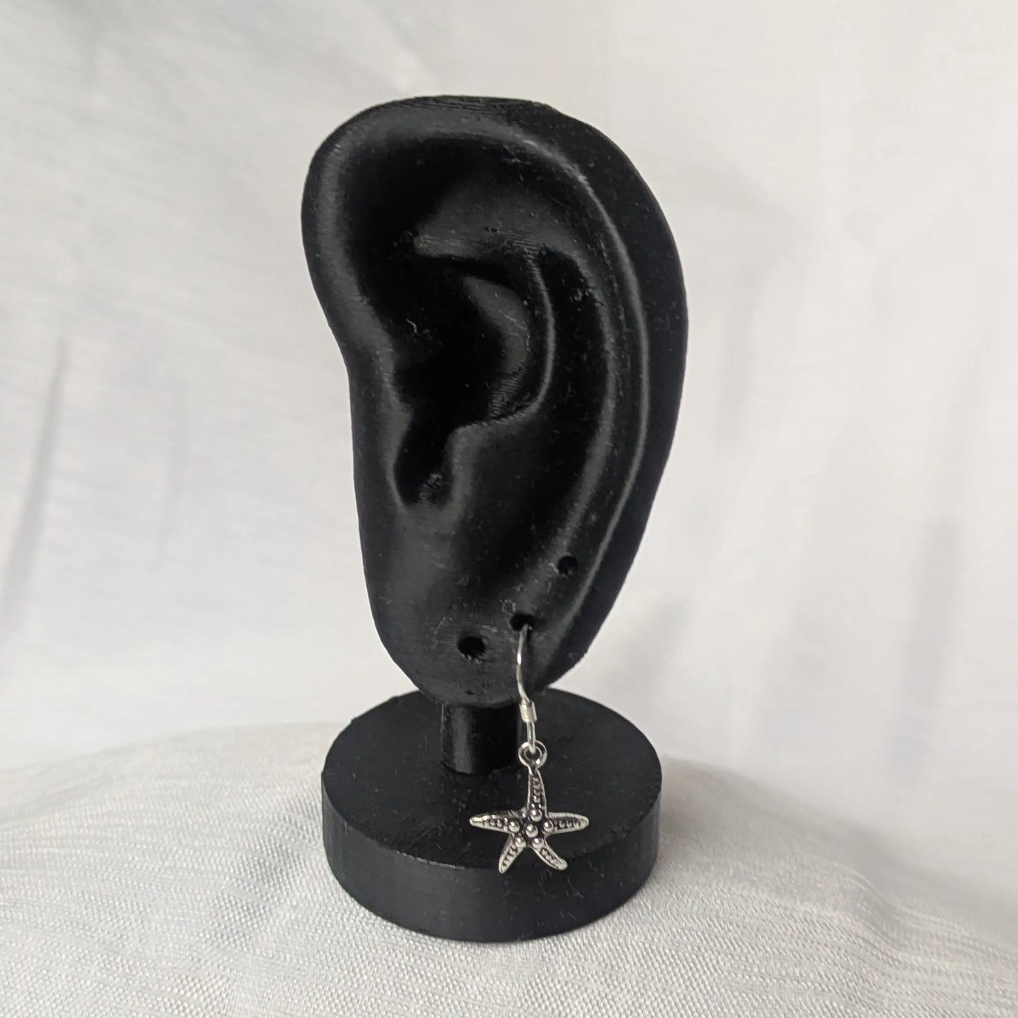 Elegante Seestern Silberohrringe präsentiert an einem schwarzen Schmuckhalter.