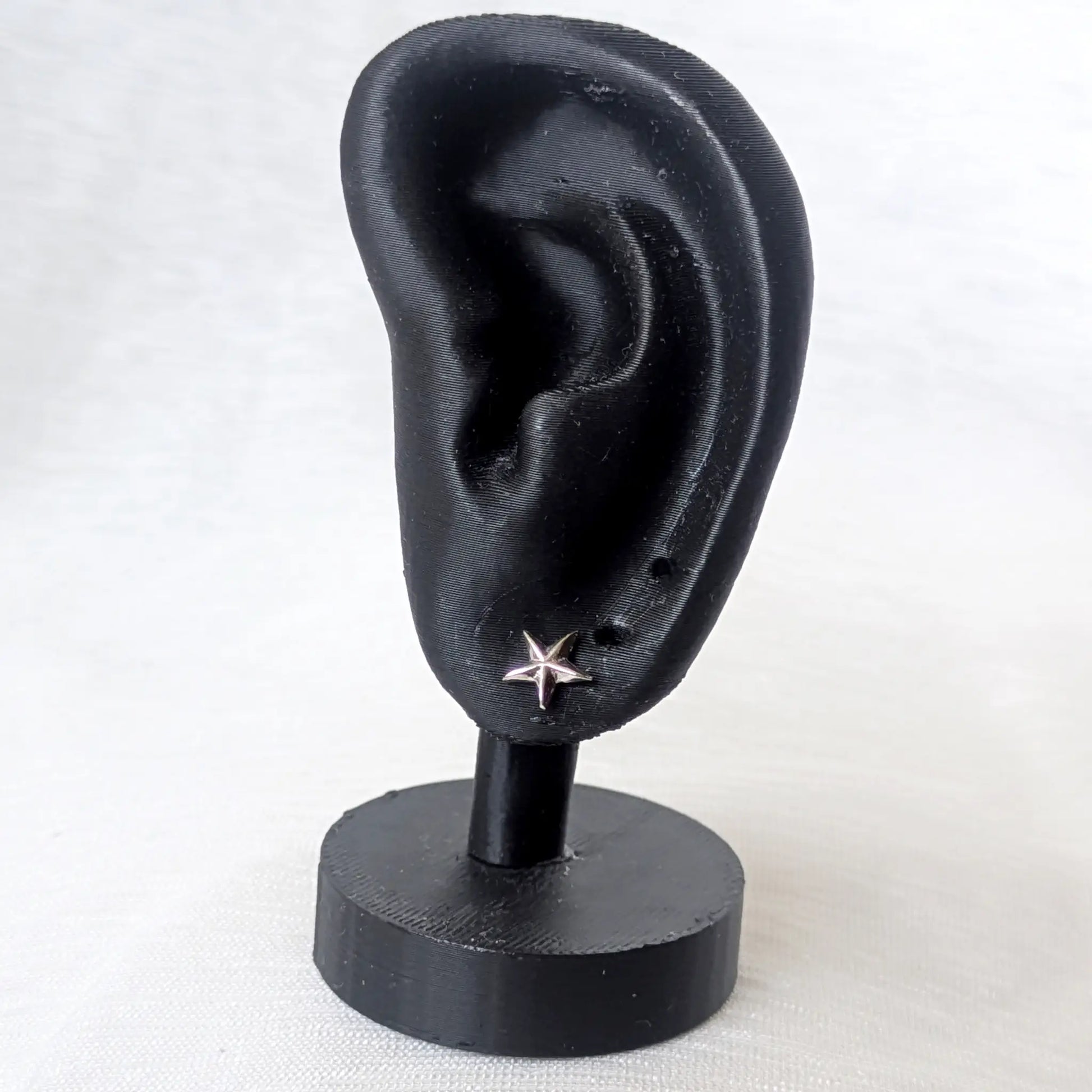 Ein kleiner, spitzer Seestern-Ohrring aus Silber, präsentiert an einem schwarzen Ohr-Display zur Größenveranschaulichung