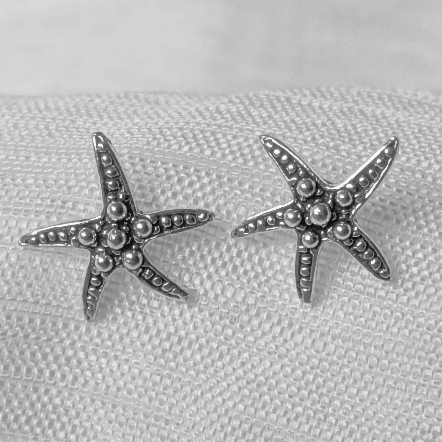 Nahaufnahme von zwei fünfstrahligen Seestern Ohrsteckern aus strukturiertem 925 Sterling Silber mit detaillierter Kugelstruktur.