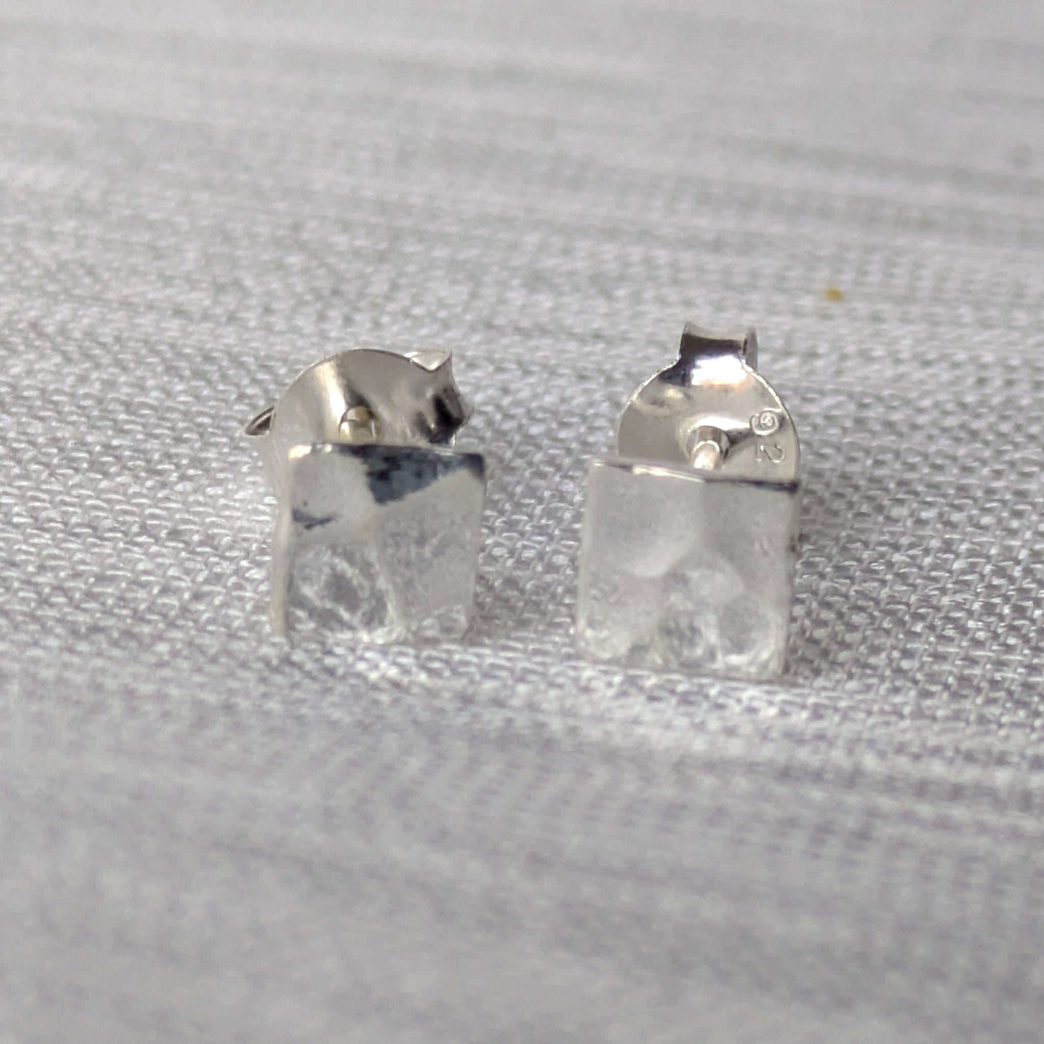 Paar minimalistischer 925-Silber Ohrstecker, quadratisch und gehämmert, frontal fotografiert.