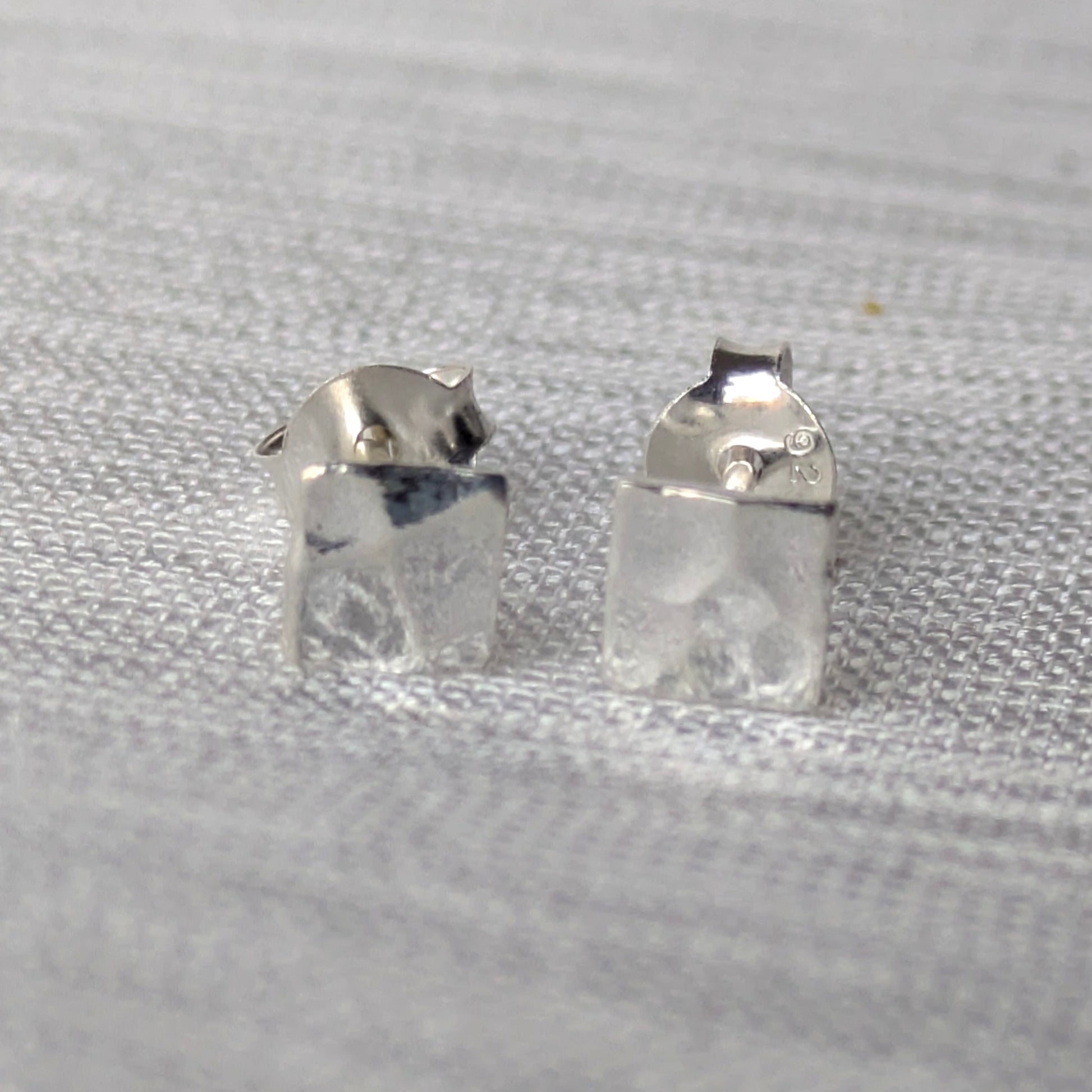 Paar minimalistischer 925-Silber Ohrstecker, quadratisch und gehämmert, frontal fotografiert.