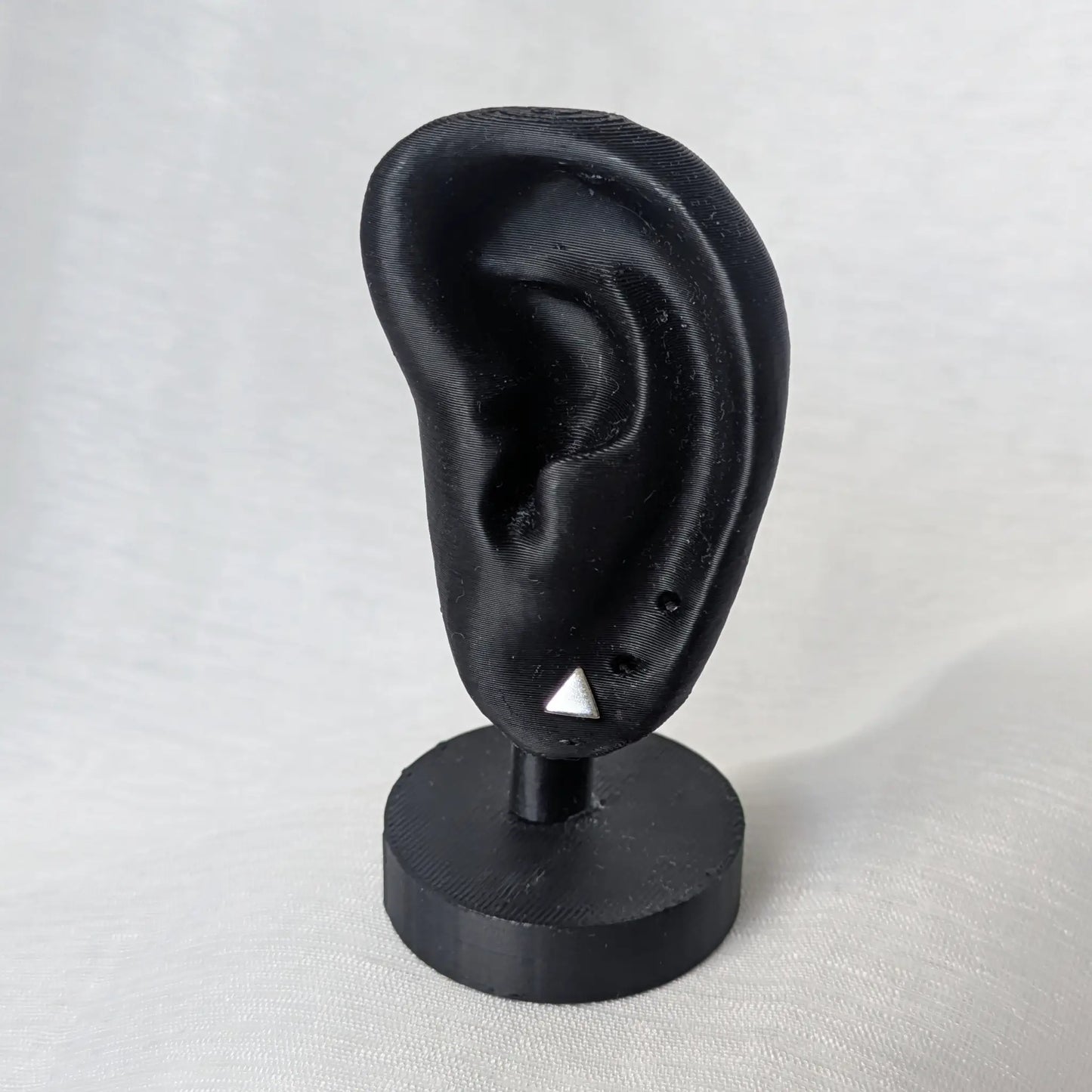 Kleine Dreieck Silberohrstecker am schwarzen Ohr-Modell zur Größenveranschaulichung.