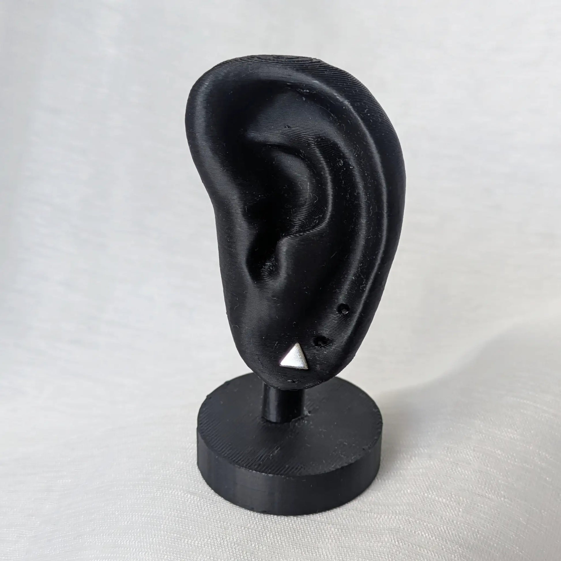 Kleine Dreieck Silberohrstecker am schwarzen Ohr-Modell zur Größenveranschaulichung.