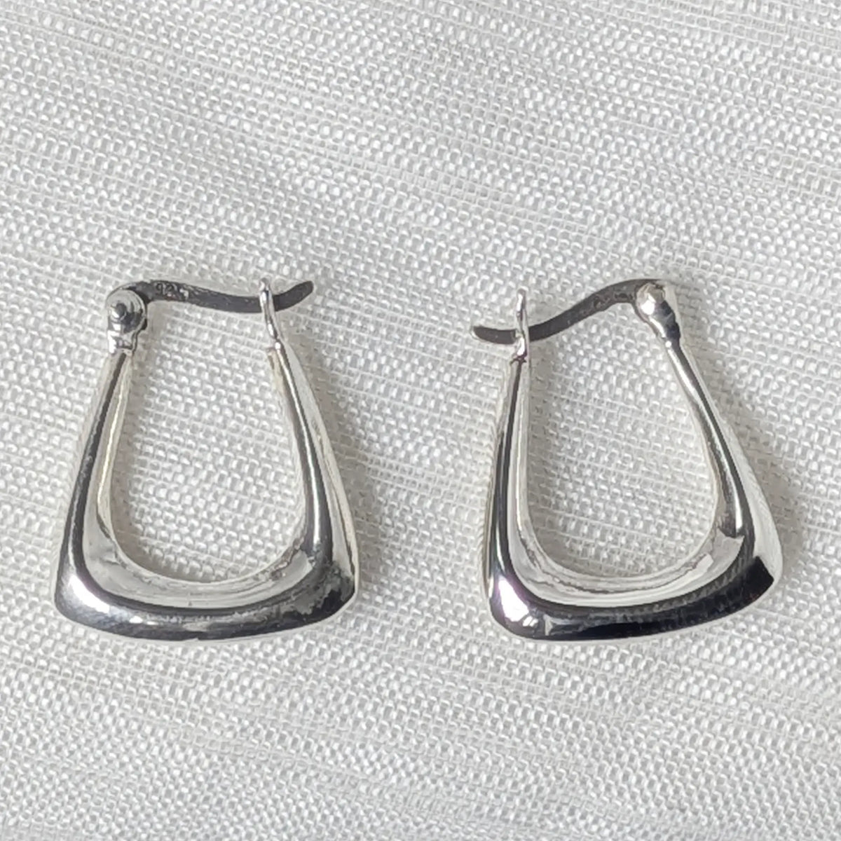 Nahaufnahme von zwei eckigen Klappcreolen aus poliertem 925 Silber im geometrischen Design.