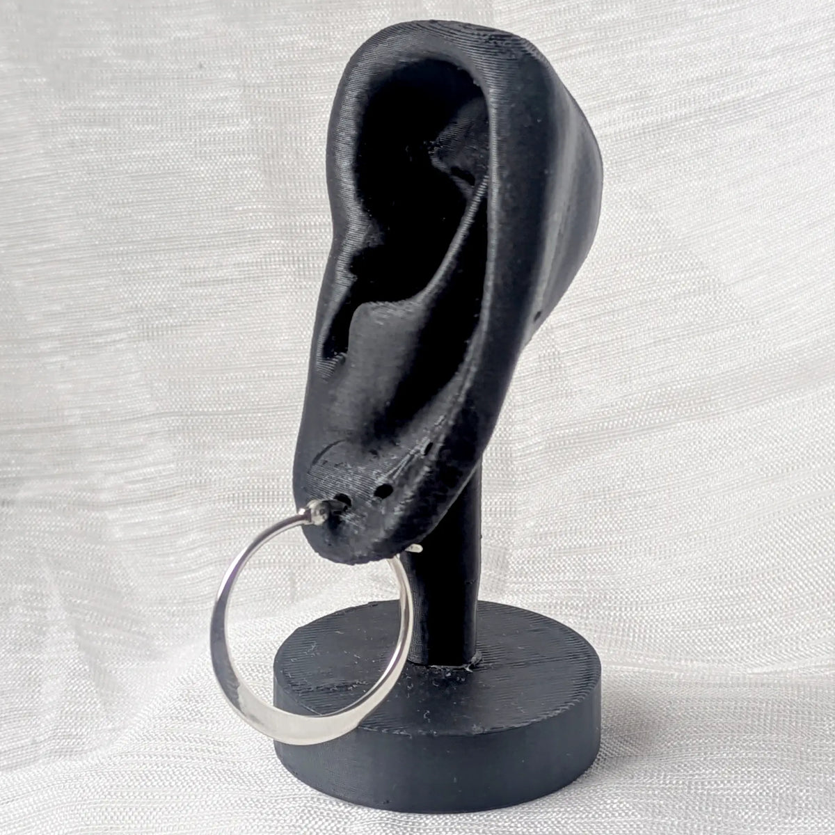 Eine moderne, unten flache 25mm Silbercreole stilvoll präsentiert an einem schwarzen 3D-Ohr-Display.
