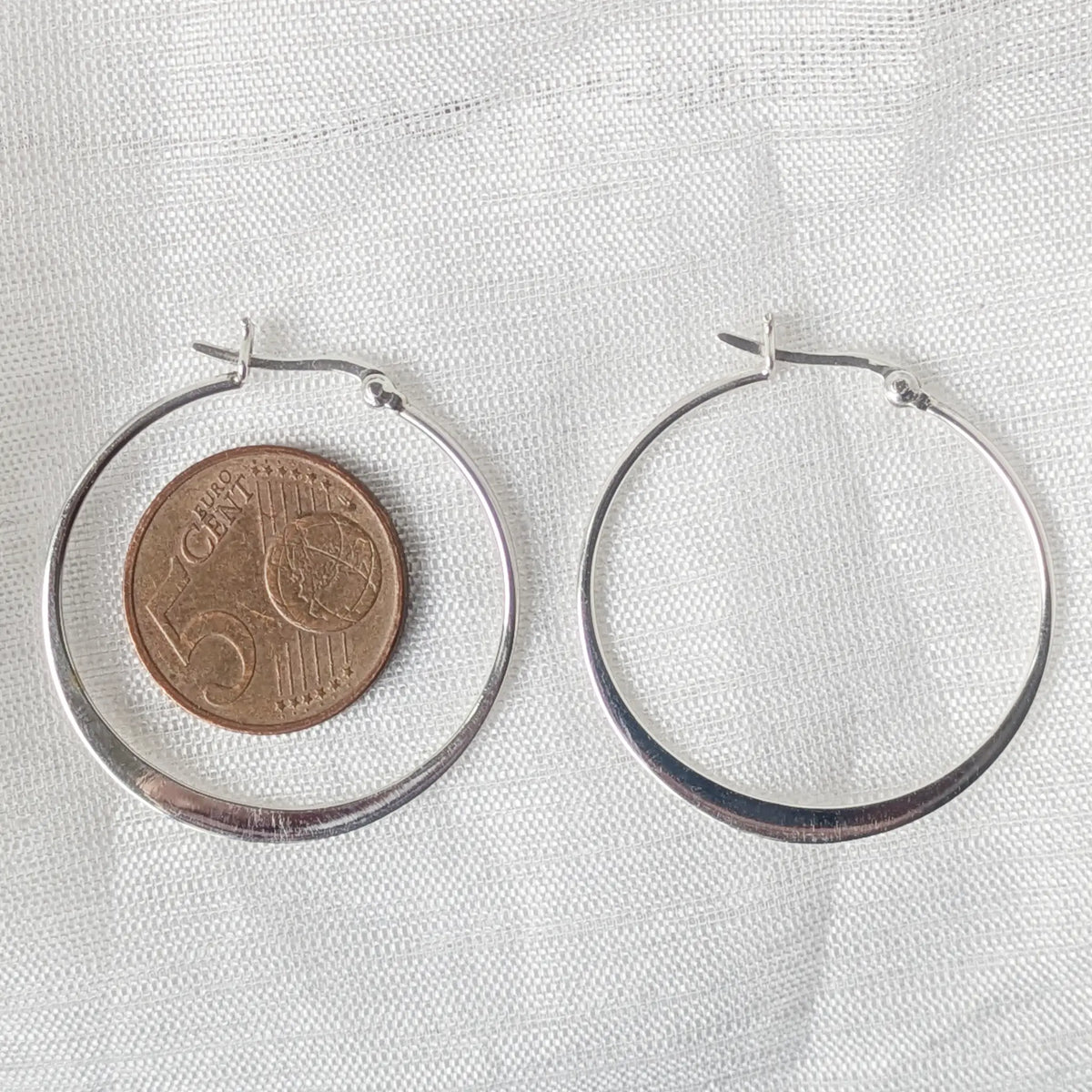Flache 925 Silbercreolen direkt neben einer 5-Cent-Münze platziert für einen klaren und realistischen Größenvergleich der 35mm Creole.