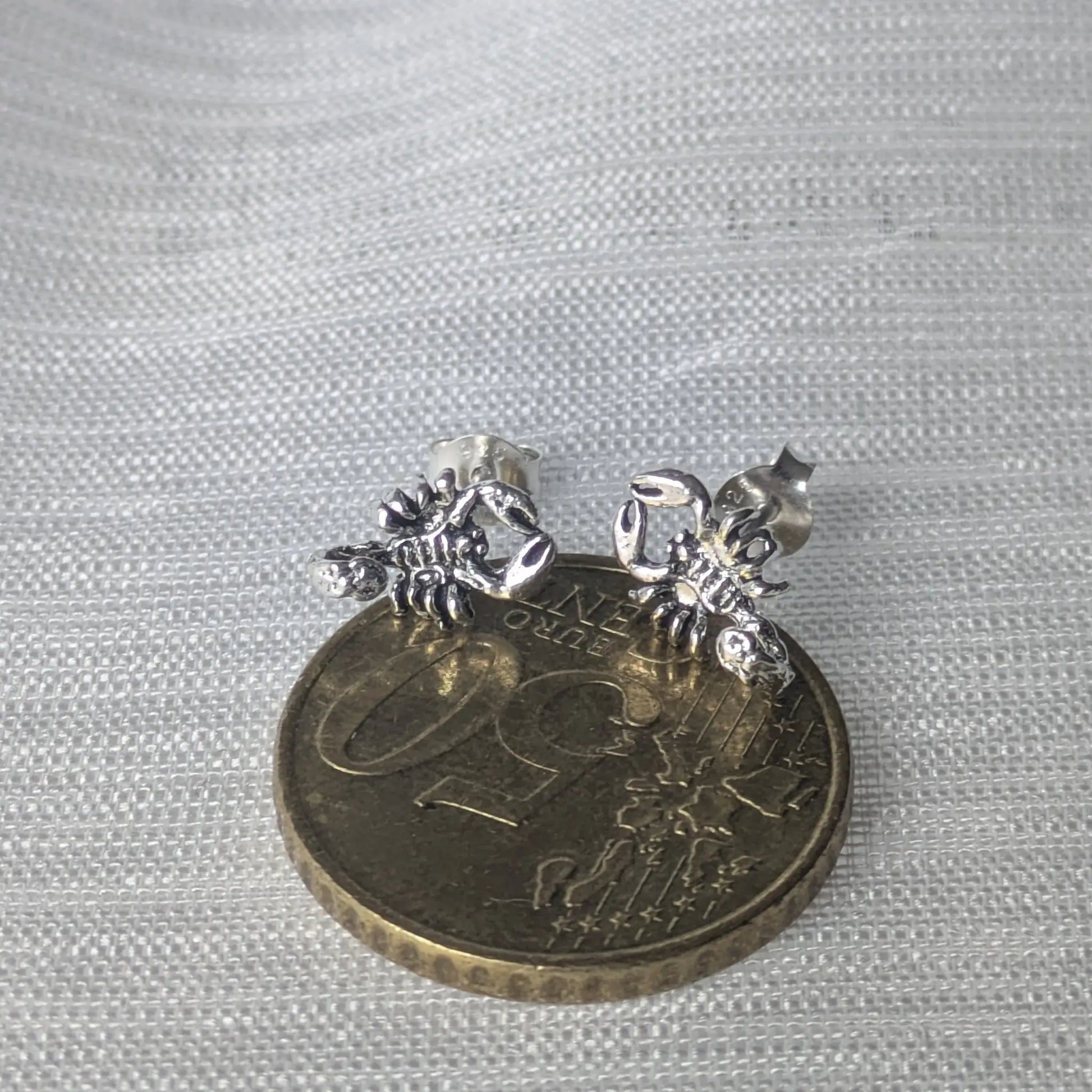 Größenvergleich der Skorpion-Ohrringe auf einer 50-Cent-Münze für eine exakte Größenvorstellung.