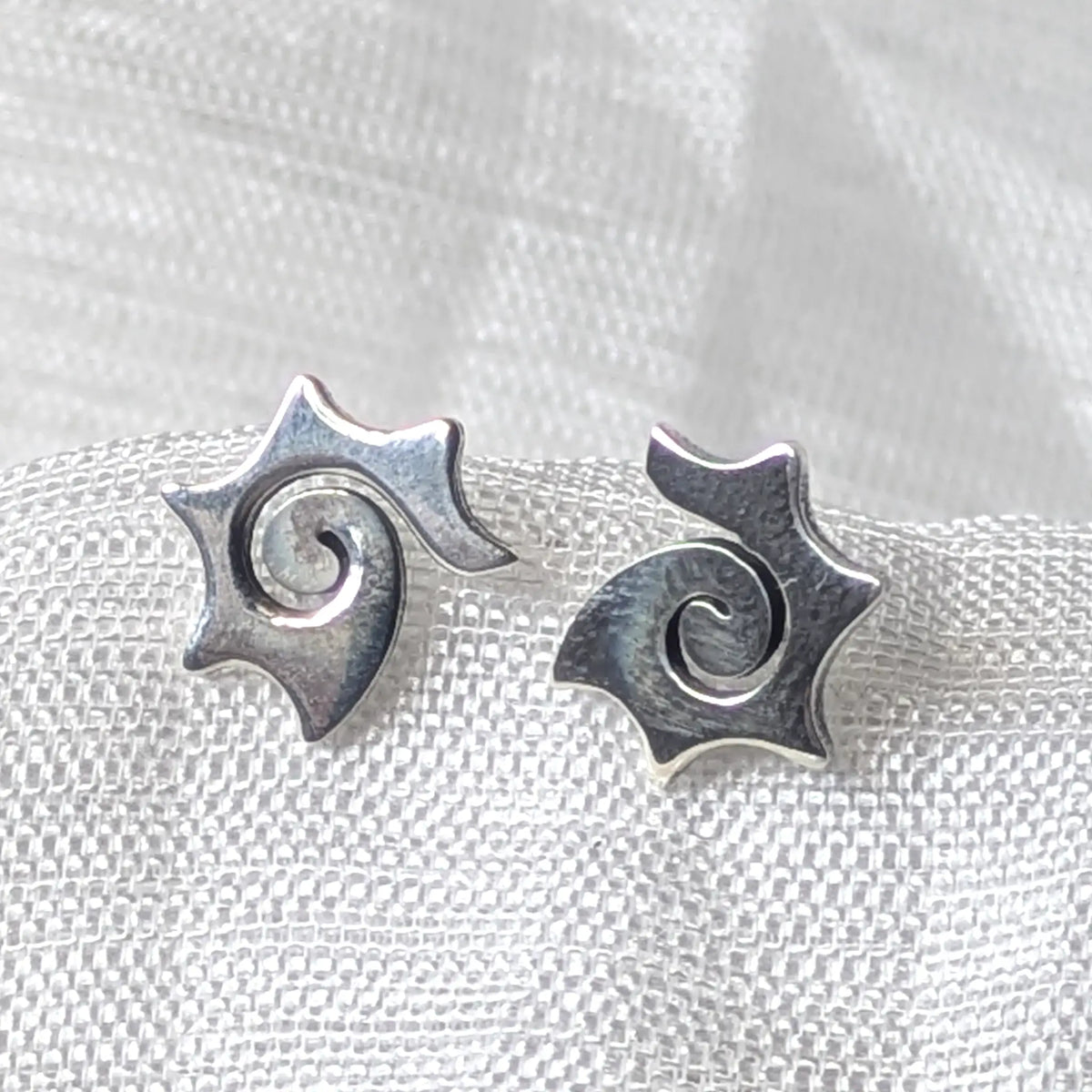Detaillierte Nahaufnahme von zwei 925 Silberohrsteckern im Design einer Sonne mit zentraler Spirale auf hellem Stoff.