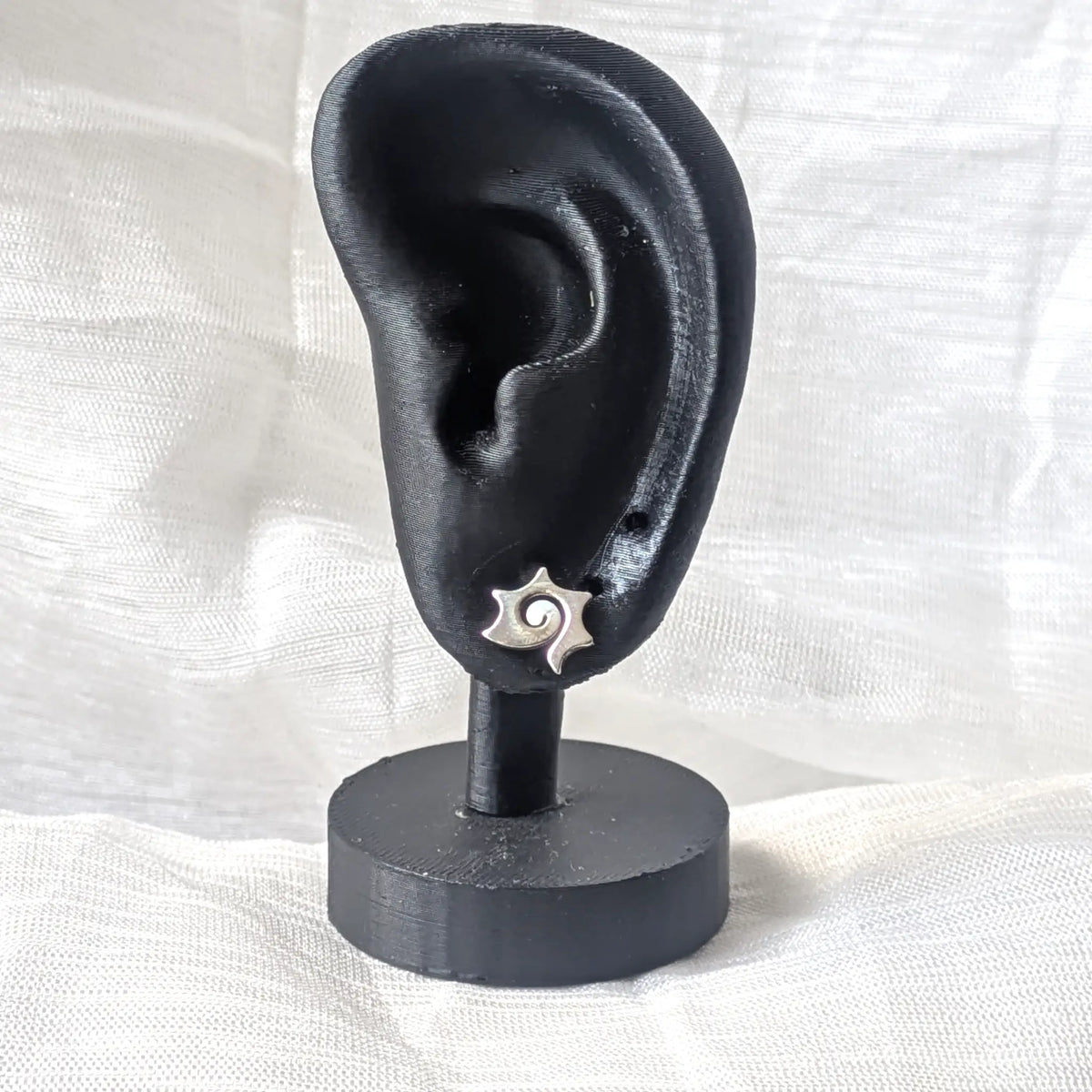  Ein einzelner Silberohrstecker mit Sonnen-Spirale, gesteckt an einem schwarzen 3D-Ohr-Display zur Anschaulichkeit der Proportionen am Ohrläppchen.
