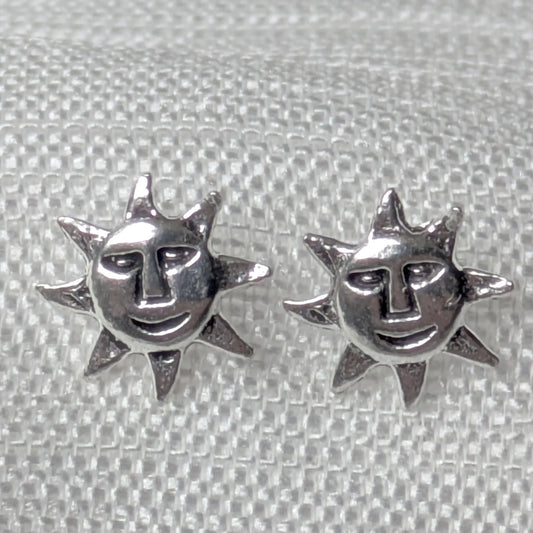 Nahaufnahme von zwei detaillierten 925 Silber Ohrsteckern mit lächelndem Sonnengesicht auf weißem Stoff