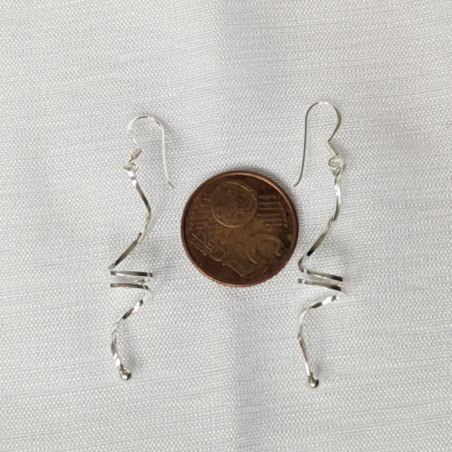 Geschwungene Silberohrringe im Größenvergleich neben einer 5-Cent-Münze.