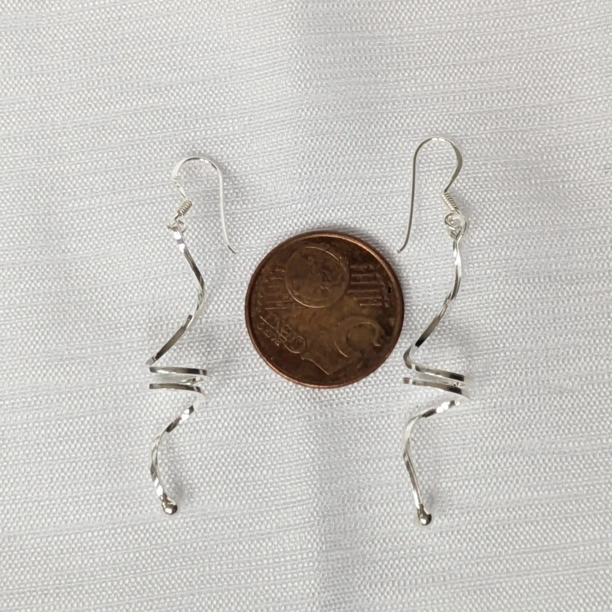 Geschwungene Silberohrringe im Größenvergleich neben einer 5-Cent-Münze.