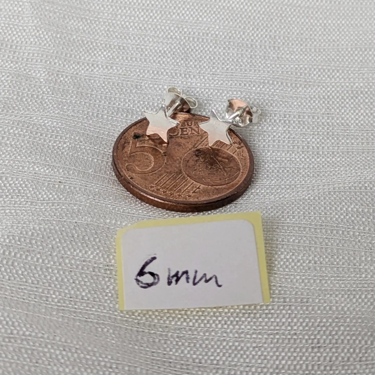 Kleine polierte 6mm Stern Silber-Ohrstecker liegend auf einer 5-Cent-Münze für den exakten Größenvergleich im Alltag.