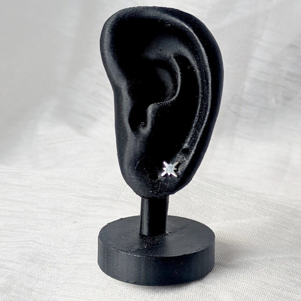 Ein matter Silber-Ohrstecker in Sternform, elegant präsentiert an einem schwarzen 3D-Ohr-Modell.