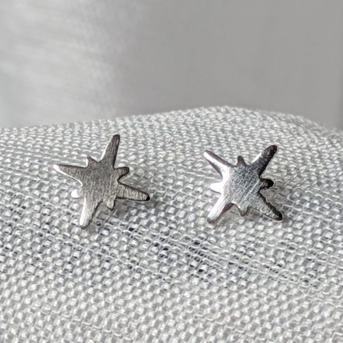 Nahaufnahme von zwei sternförmigen 925 Silber Ohrsteckern mit strukturierter, eismatter Oberfläche.