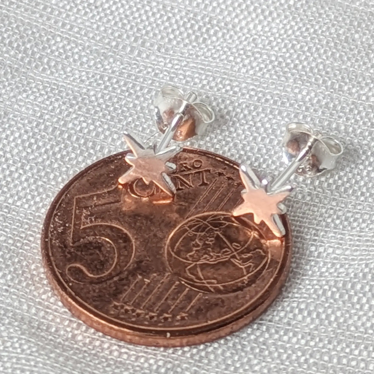 Größenvergleich eines filigranen 925 Silber Stern-Ohrsteckers, der flach auf einer 5-Cent-Münze liegt.