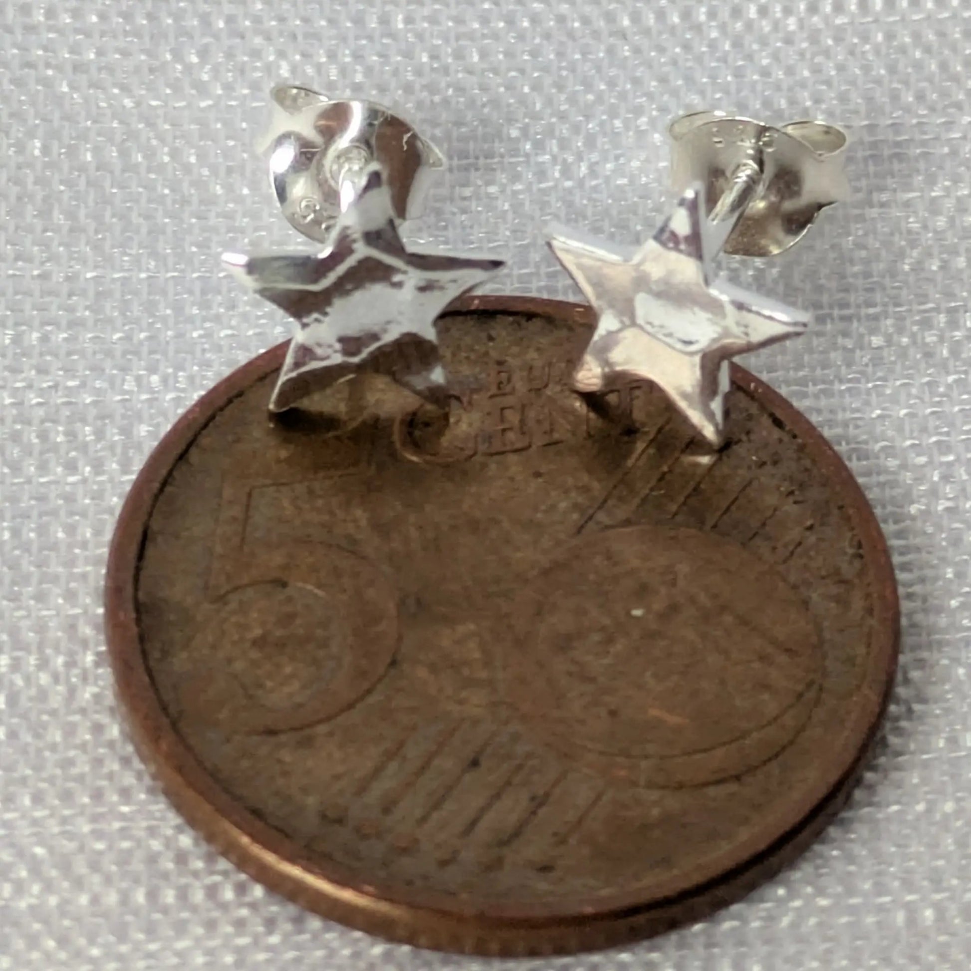 Größenvergleich der silbernen Stern-Ohrstecker auf einer 5-Cent-Münze zur präzisen Einschätzung der Maße.