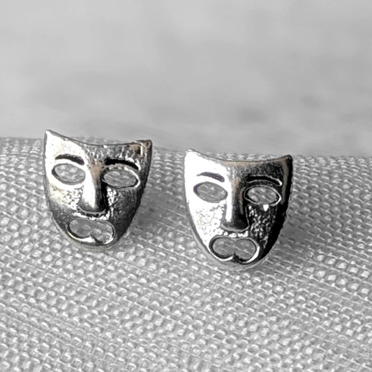 Detailreiche Nahaufnahme von zwei hochglanzpolierten Theatermasken Ohrsteckern aus 925 Sterling Silber mit dem Motiv der Tragödie.