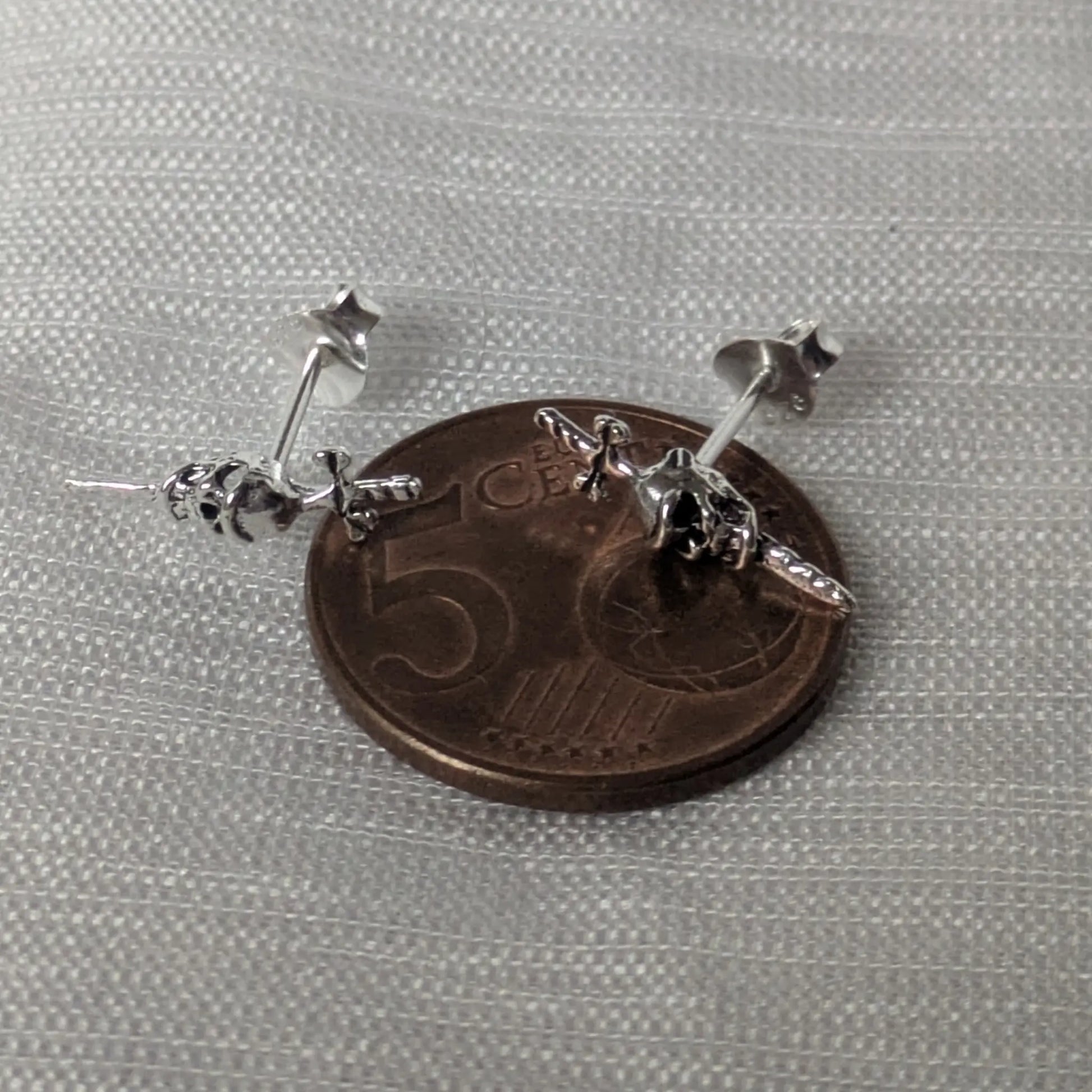 Größenvergleich der silbernen Skull-Ohrstecker auf einer Münze.